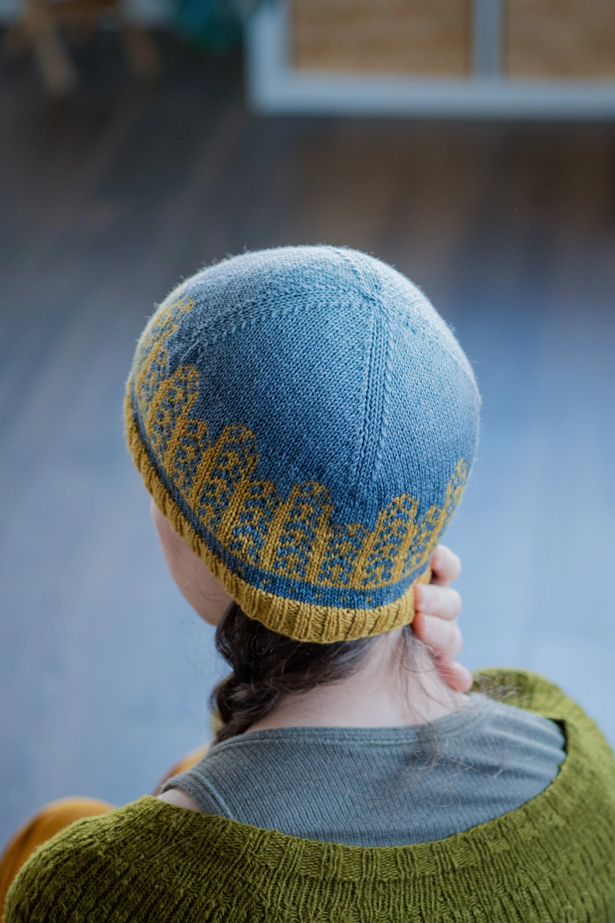 View from behind of Andrea wearing a toque with a yellow colour motif and fading blue background.