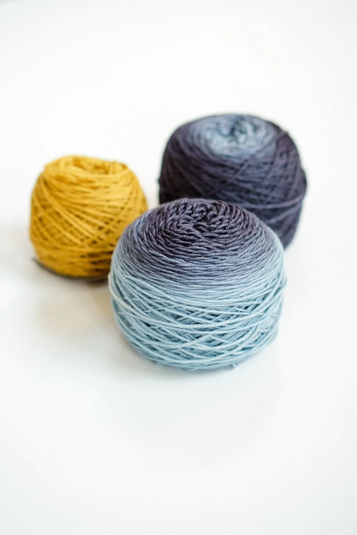 Three balls of yarn — one yellow and two blue fading.