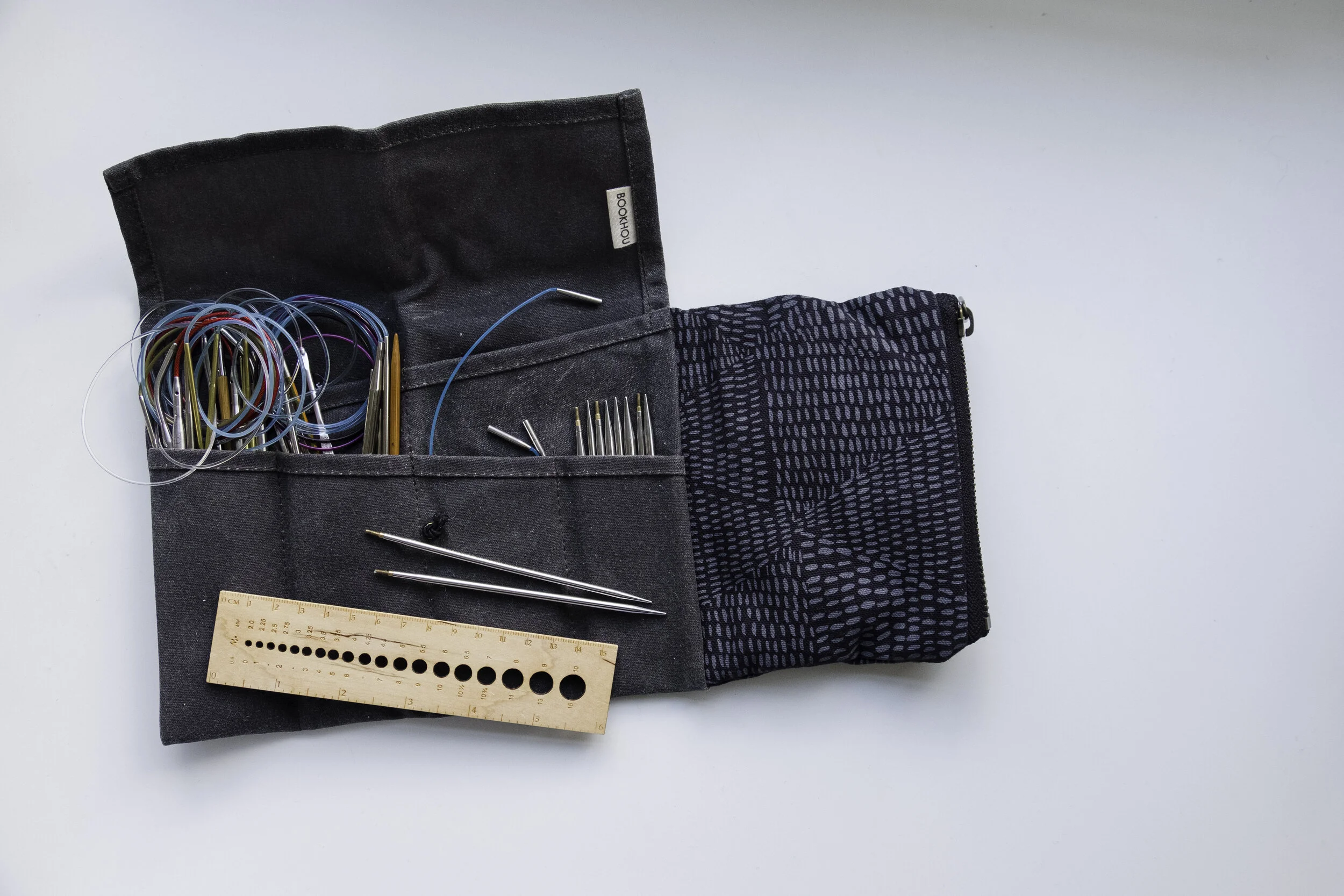 A dark blue tool roll with a wooden needle gauge and a set of interchangeable needle tips laid on it.