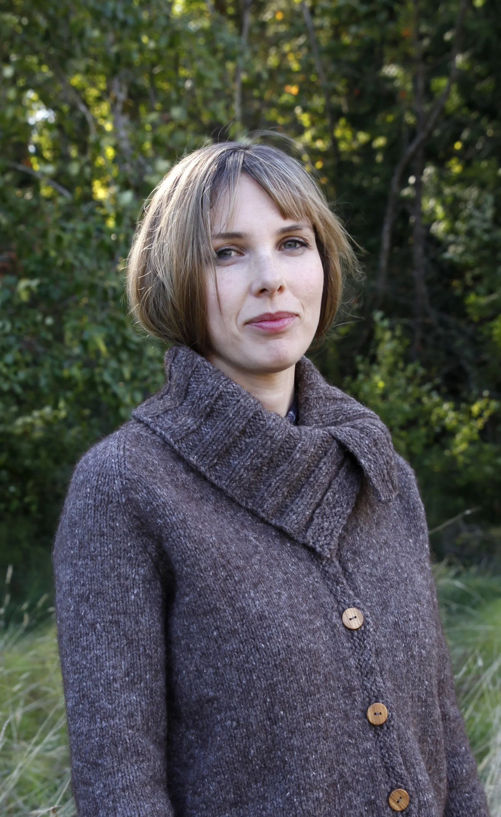 A young white woman wearing a brown sweater with a big, folded-over cowl is smiling at the camera.