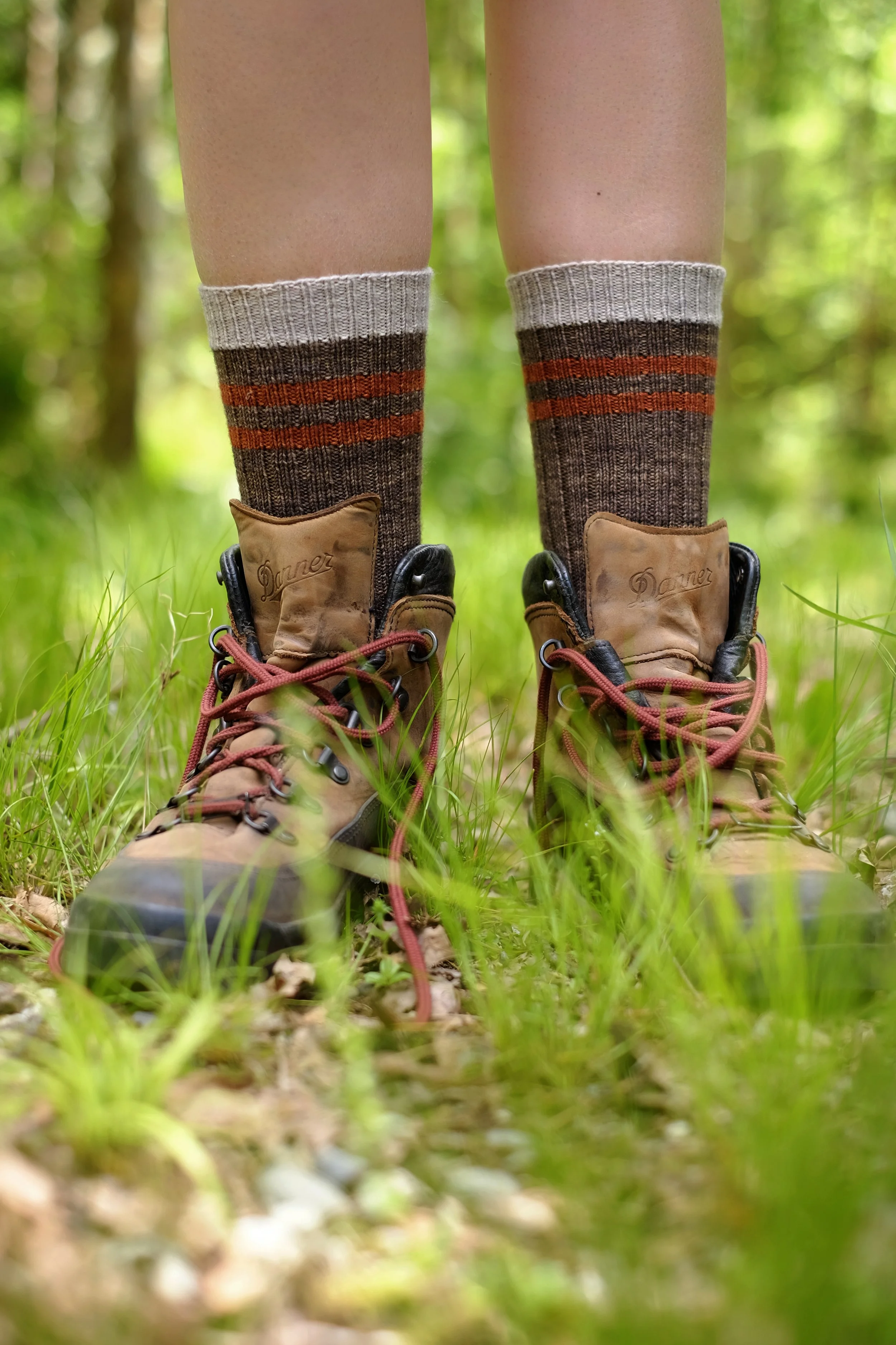 Feet in dark grey socks with orange and pale grey stripes and hiking boots in a verdant green setting.