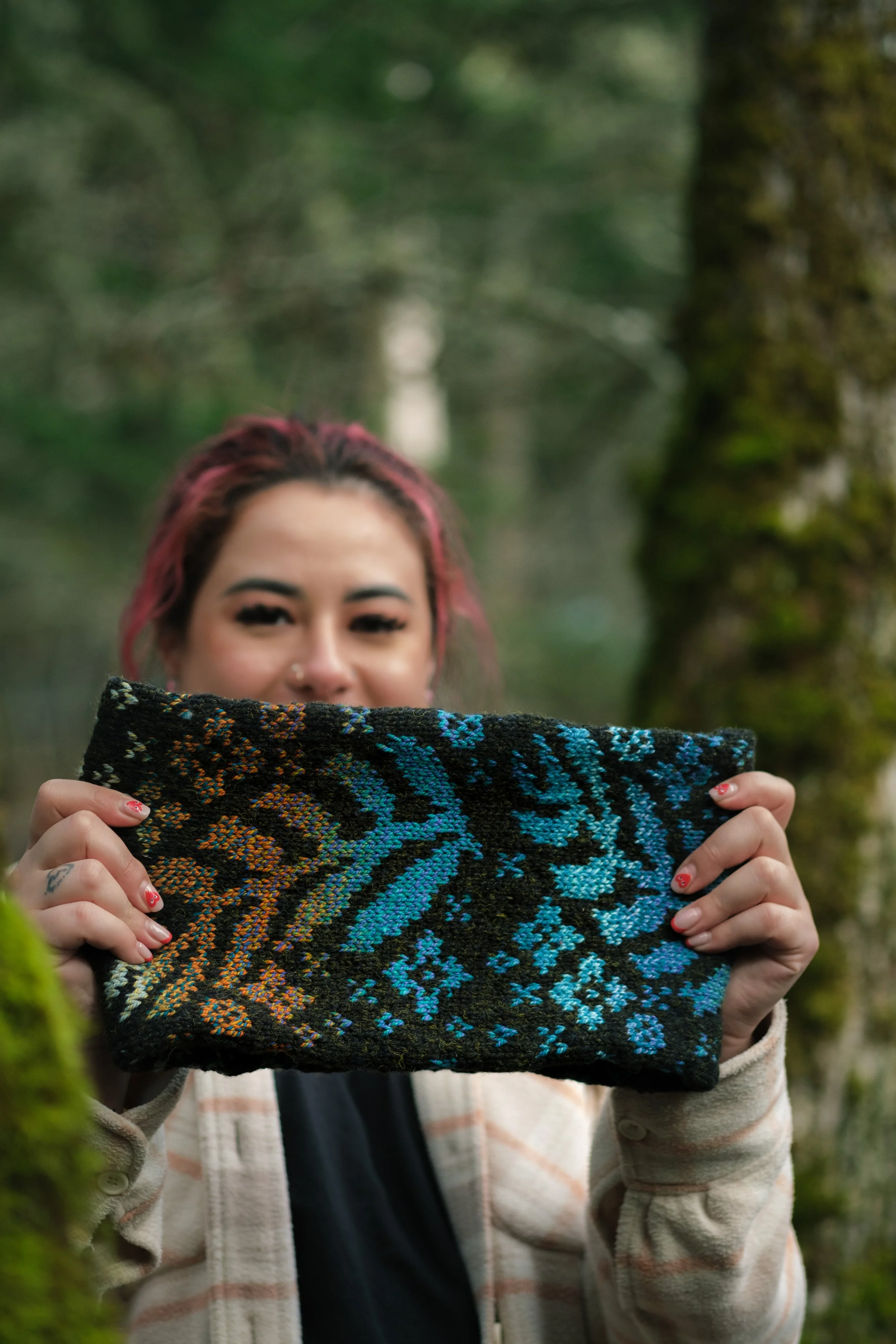 Pauline holding up the cowl in front of her. The colourwork is gradient shades of teal, orange, and pale green.