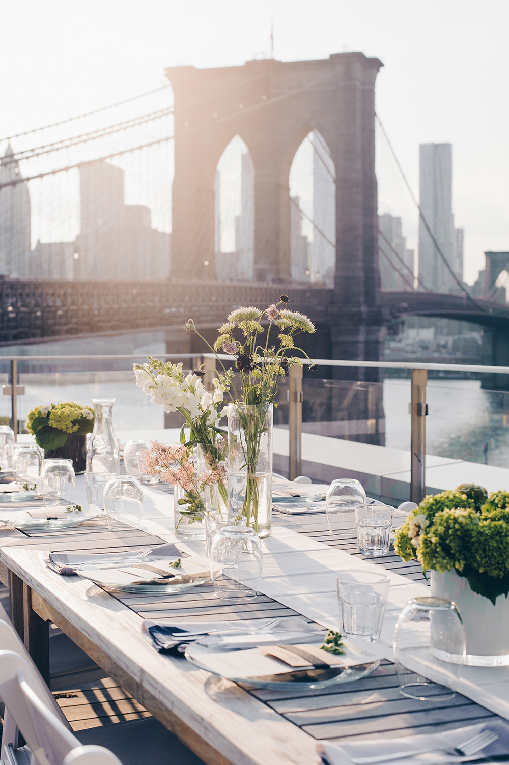 Beautifully set rooftop dinner table at sunset with the Brooklyn Bridge in the background