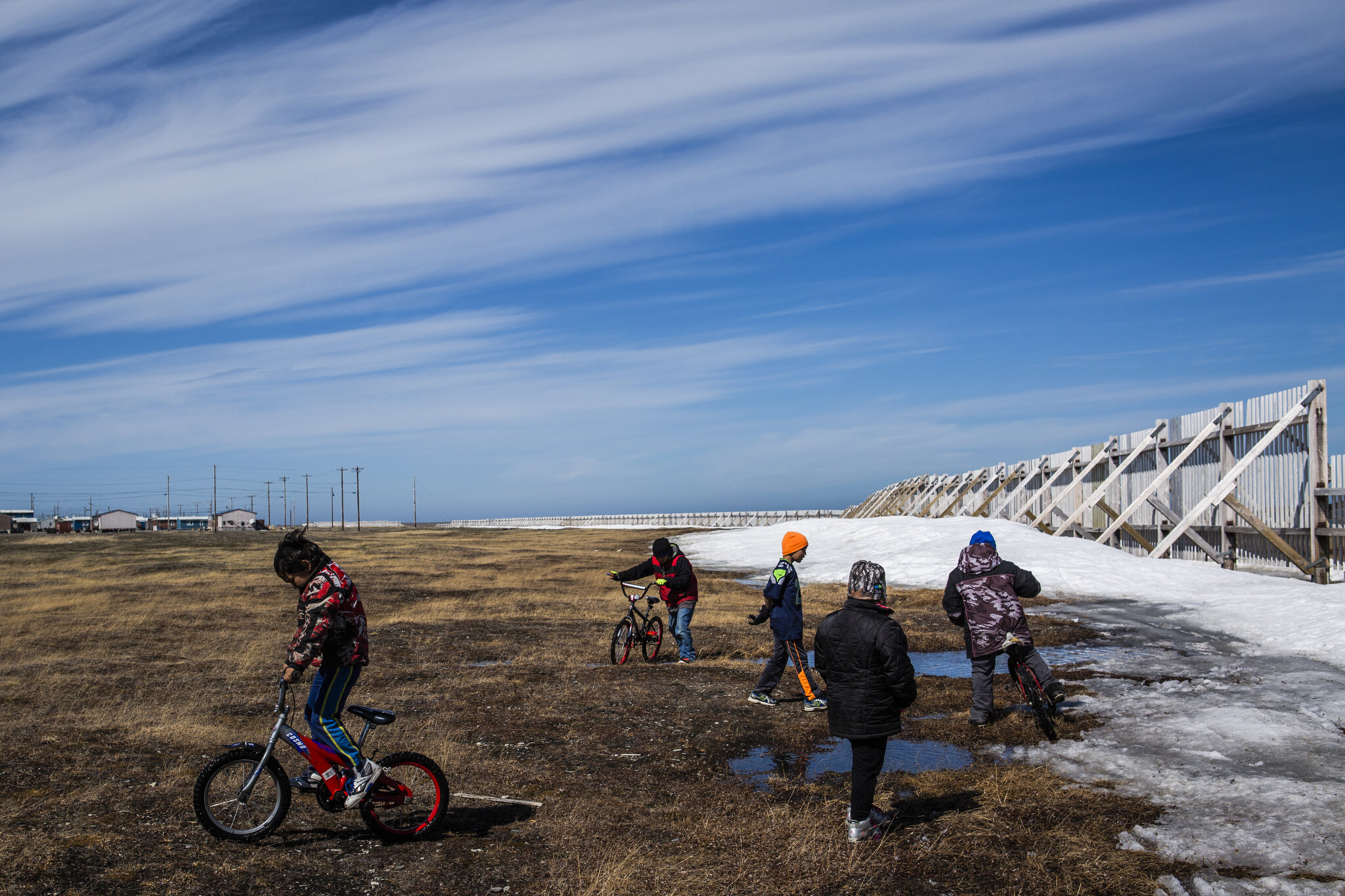  Children play along the edges of the annual whaling feast celebration in Point Hope, Alaska. To the children’s right lies a snow fence meant to protect from winter storm surges engulfing the village, and underneath their feet rests an invisible thre