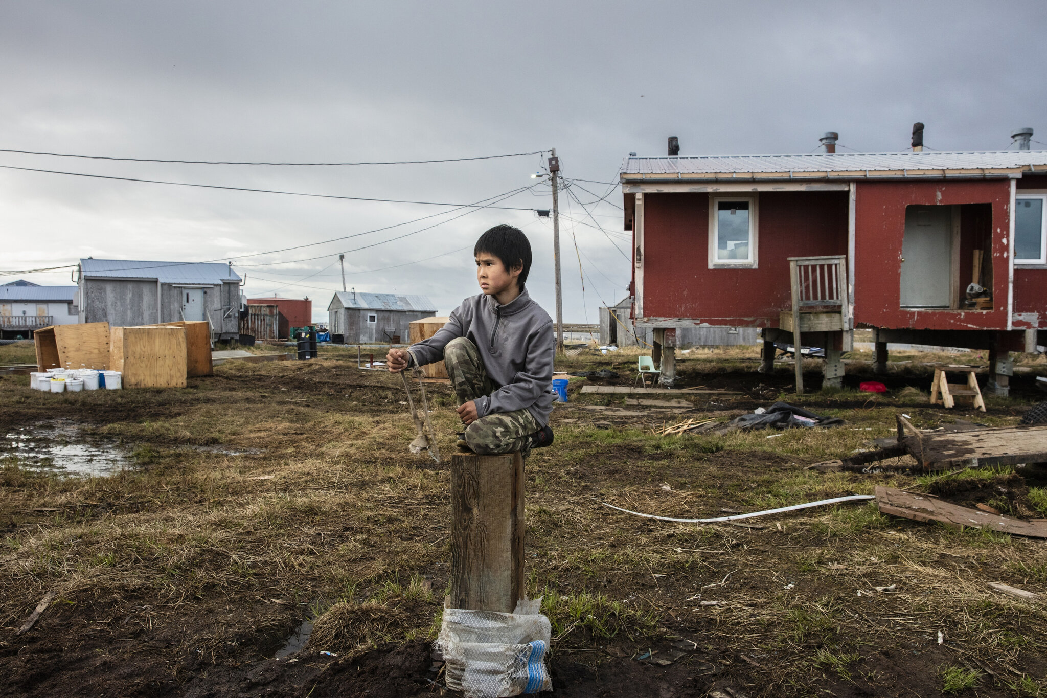  Reese John plays with his slingshot on a piling from a recently demolished home in Newtok, Alaska. May 28th, 2019. Just a few dozen feet away are crumbling cliffs of permafrost falling into the Ninglik River. Erosion has already gobbled up approxima