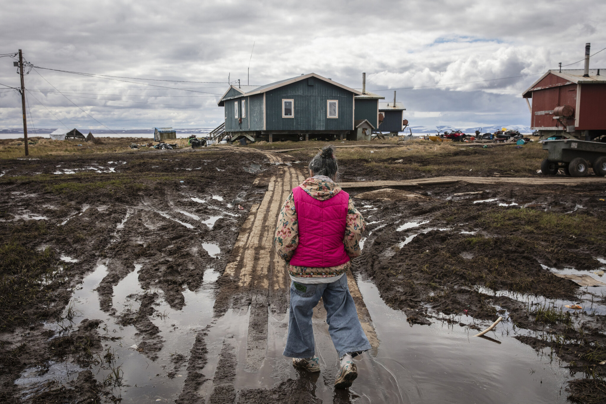  Monica Kasayuli walks across a flooded walkway on her way home in Newtok, Alaska. May 26th, 2019. Her home was deemed unsafe and she was packing at the time to move to temporary FEMA housing, before becoming one of Newtok's "pioneers." Currently Mon