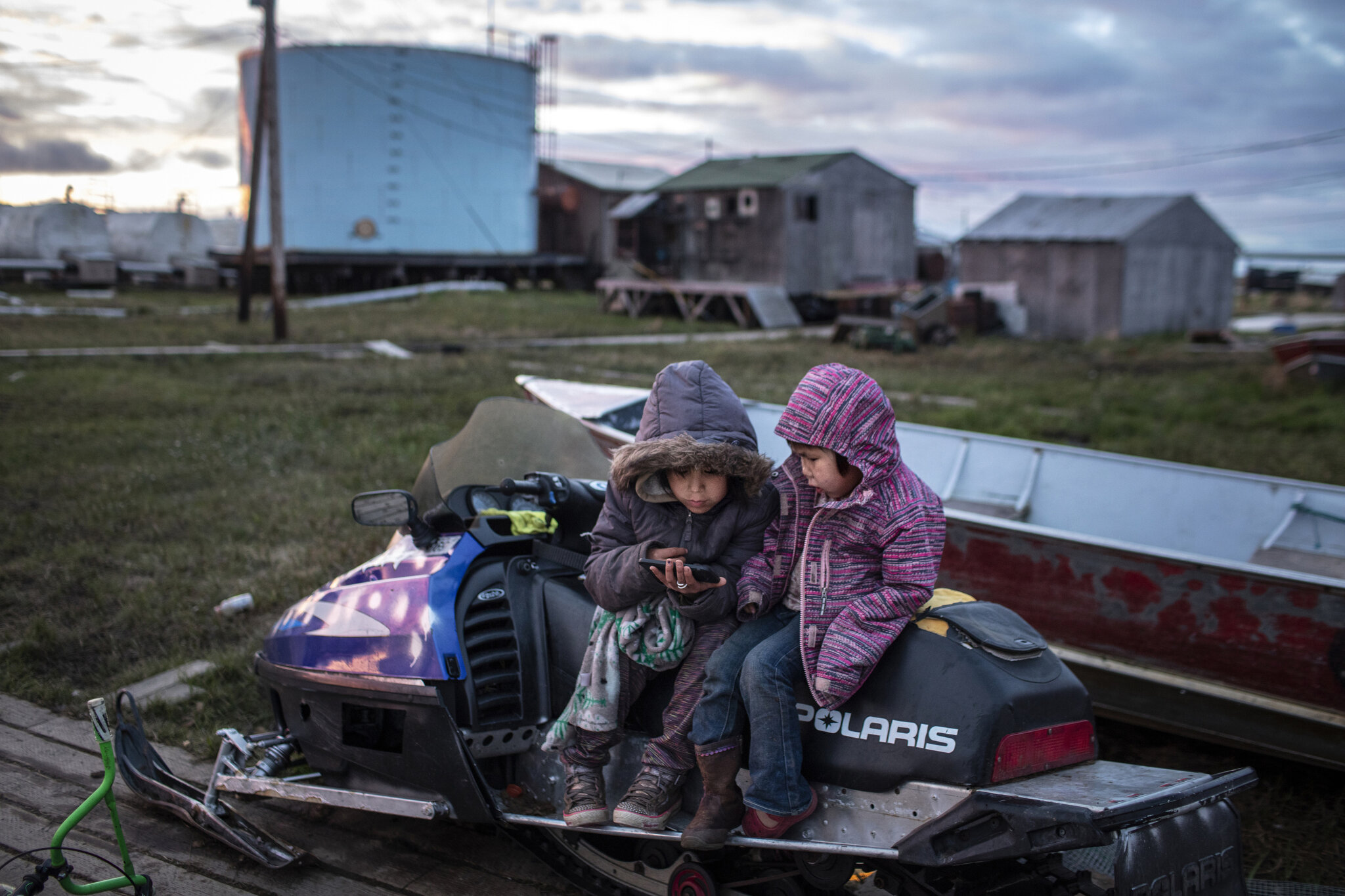 Two young girls play on a family member's phone while sitting on a broken down snowmobile in Newtok, Alaska. Smart phones are ubiquitous in the village. June 2, 2019.The Yupik village of Newtok, Alaska, population 380, is sinking as the permafrost b