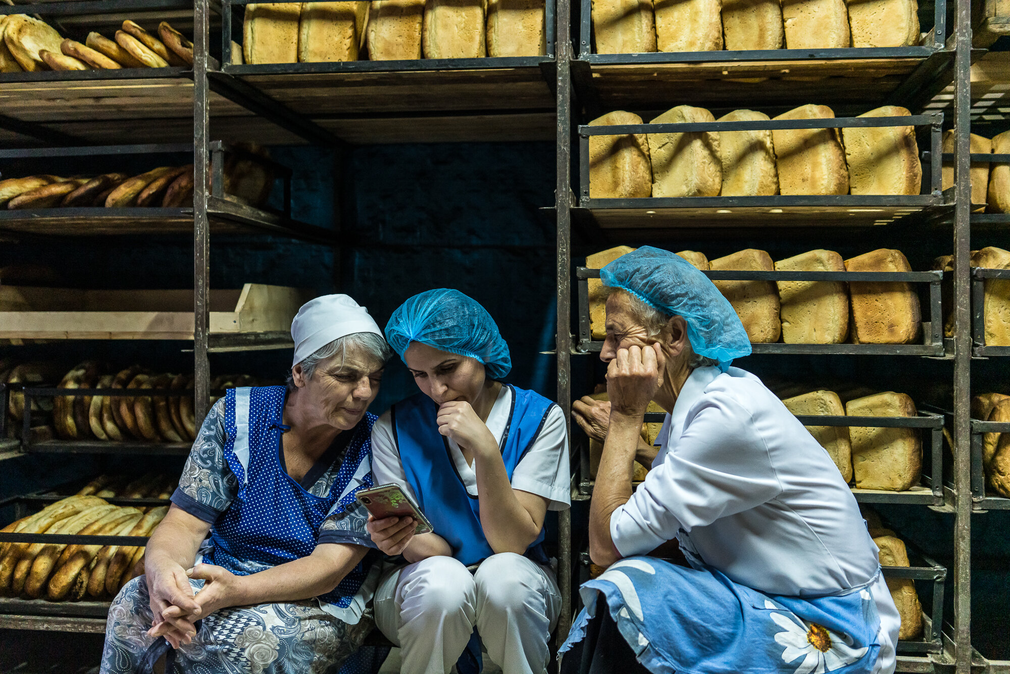  Workers at the Karavay bakery watch an online video report about the ongoing war during a break from baking bread for members of the Armenian military in the front-line city of Martakert. Stepanakert, Nagorno-Karabakh. 2020. 