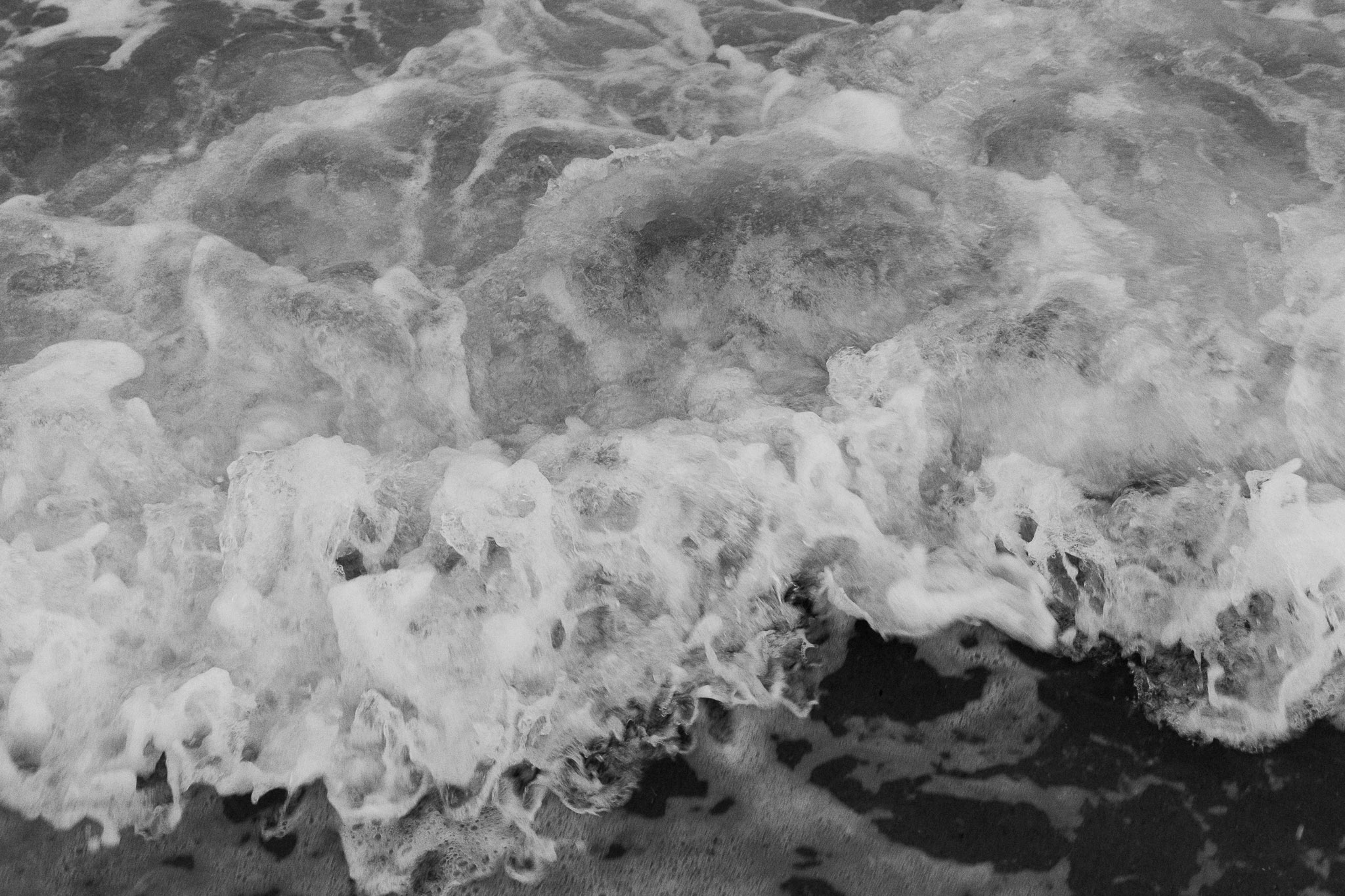 An aerial-type black and white photograph of waves, taken by standing close to the ocean and looking down.