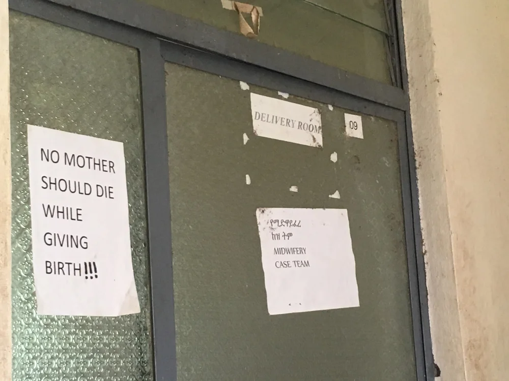 The door to the delivery room- inside, a mother was in labor, assisted by a midwife working with basic supplies