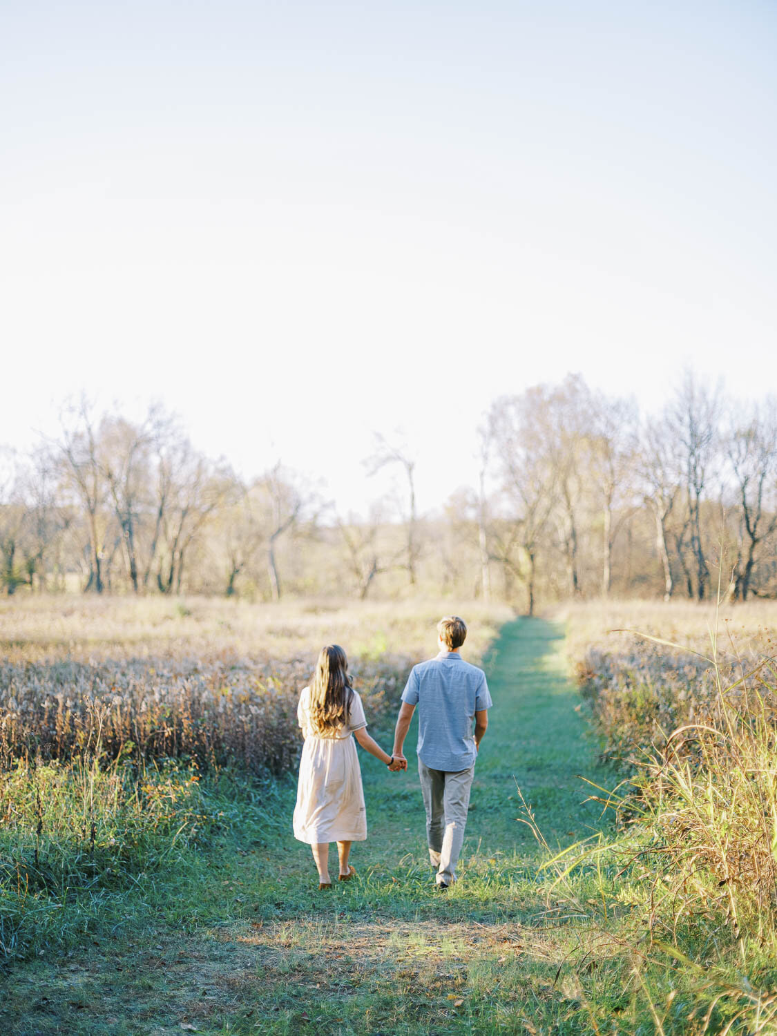 man-and-woman-walking-through-field-during-golden-hour-for-their-fall-engagement-session.jpg