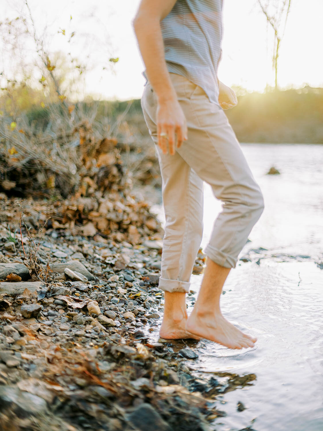 man-rolling-up-slacks-to-wade-in-rivanna-river-during-golden-hour-at-his-engagement-session-in-charlottesville-virginia-2.jpg