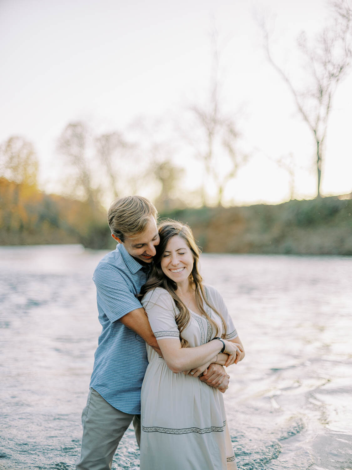 hugging-woman-from-behind-while-standing-in-rivanna-river-during-fall-engagement-session-at-golden-hour-in-charlottesville-virginia.jpg