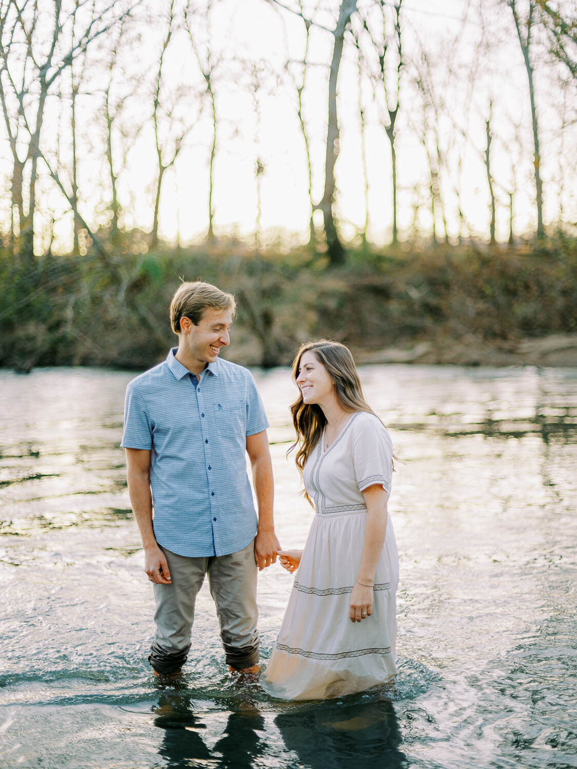 man-holding-woman's-hand-while-standing-in-rivanna-river-during-fall-engagement-session-at-golden-hour-in-charlottesville-virginia.jpg