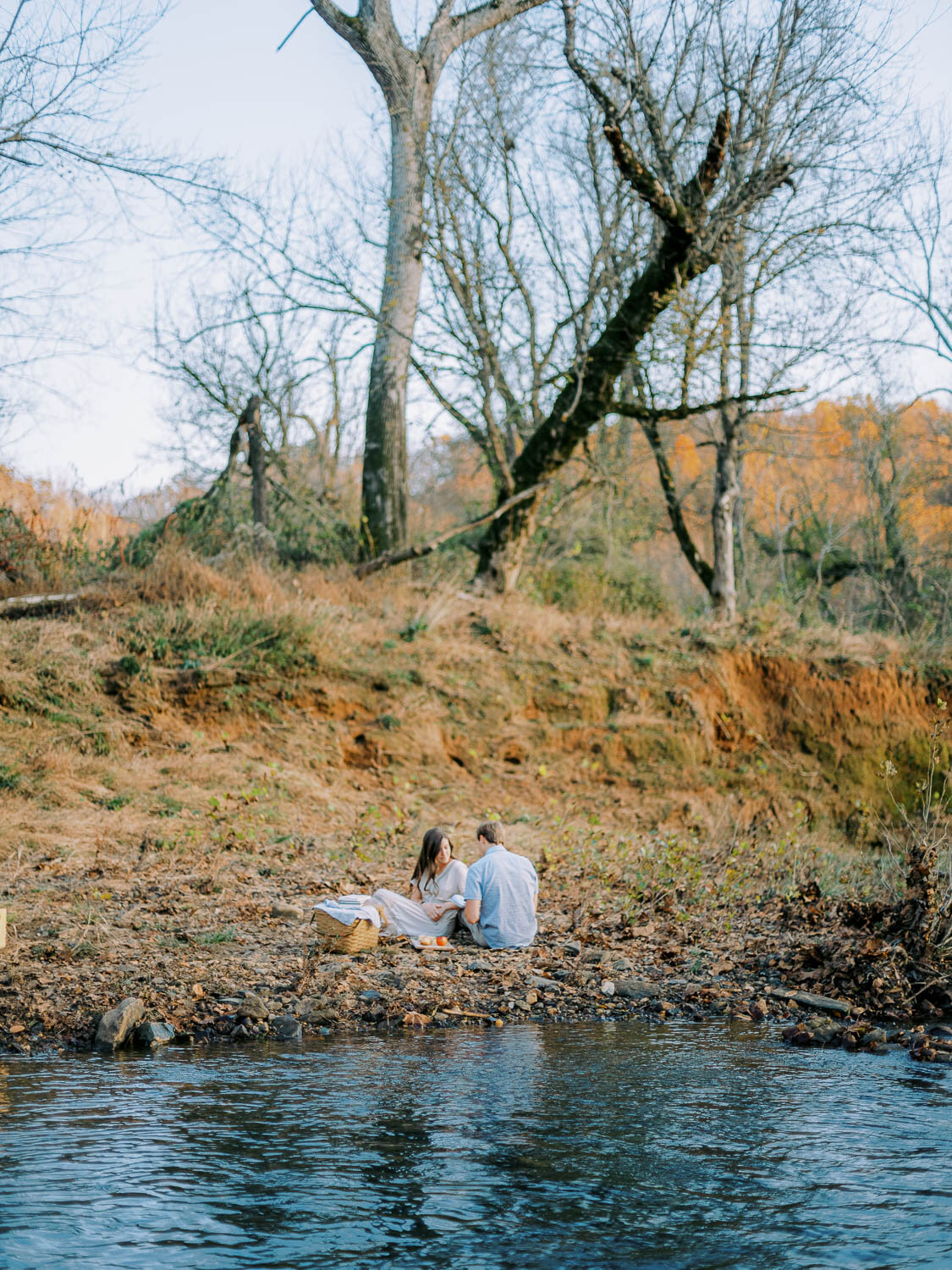 woman-and-man-sit-on-riverbank-during-engagement-session-in-charlottesville-virginia.jpg