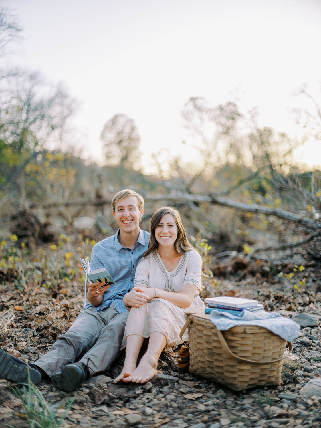 woman-and-man-smile-while-sitting-down-on-riverbank-during-engagement-session-in-charlottesville-virginia.jpg