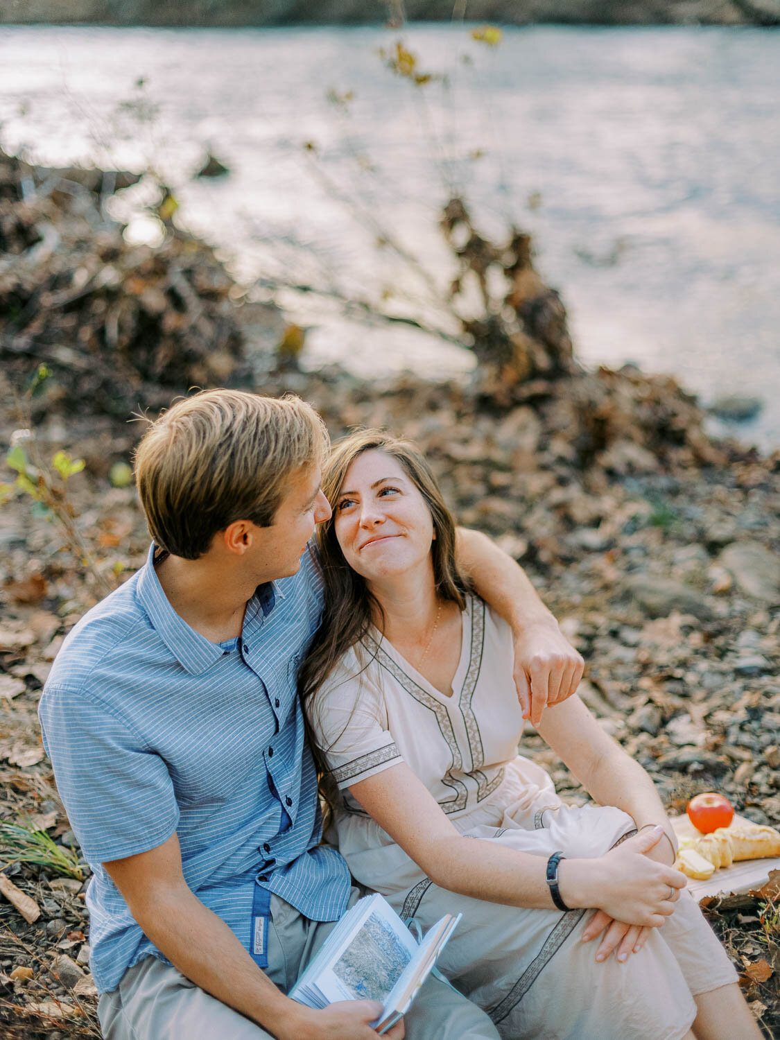 woman-tenderly-looking-at-man-while-sitting-side-by-side-on-riverbank-during-engagement-session-in-charlottesville-virginia.jpg
