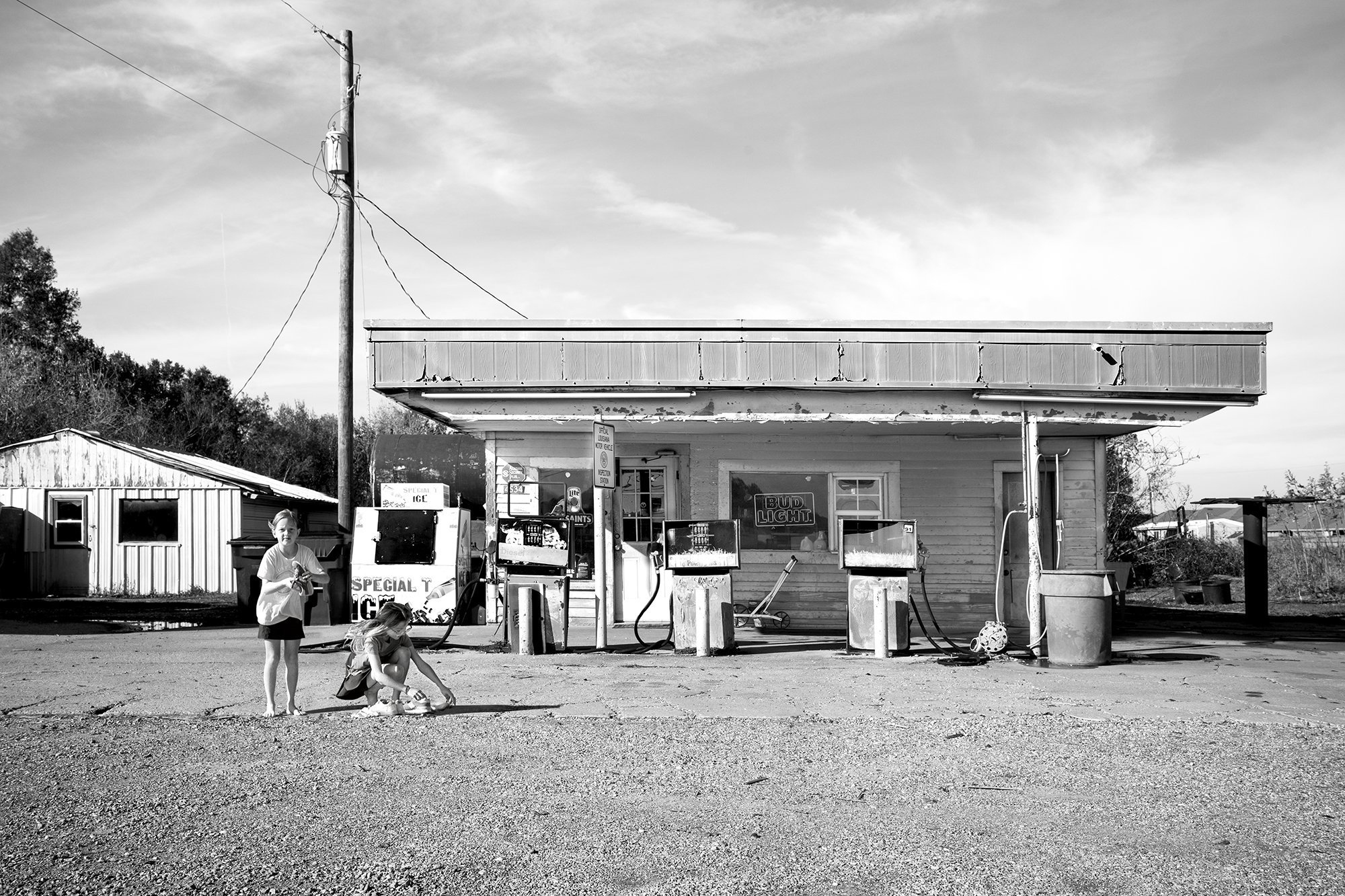 Two girls cleaning their shoes in front of a gas station, Abbeville, Louisiana, USA