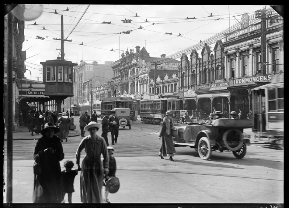 1919: Trams ruled. Looking north east from the southern corner of Wellesley Street West and Queen Street, Auckland Central showing pedestrians, cars and trams in the street, with the premises of Smith and Caughey on the left, and the east side of Queen Street between Wellesley and Victoria Streets, with a tramway control cabin on the corner of Wellesley Street West and Queen Street, the Fountain of Friendship buildings, the Majestic Theatre and Edson's Buildings and the premises White's Belgian Lounge, James Pascoe Jewellers, G W Wright, Pastry Cook and Tea Rooms, J H Dalton City Tailoring Establishment; Samuel Barry (Optician) and Cruickshank and Miller, Ironmongers (Photo Sir George Grey Special Collections, Auckland Libraries, 4-7643)