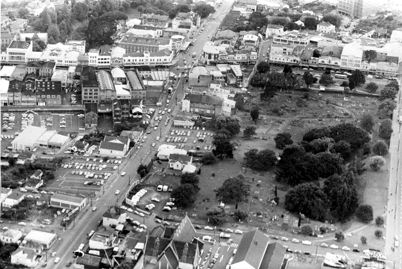   1964 VIEW: Looking north over part of Symonds Street Cemetery, now partly occupied by the Northern Motorway, showing Upper Queen Street, (vertically centre left), Queen Street (top centre), Karangahape Road, left to right (top), Alex Evans Street (formerly East Street), (bottom), with St Benedicts Church (foreground) (Photo: Sir George Grey Special Collections, Auckland Libraries, 580-10446)  
