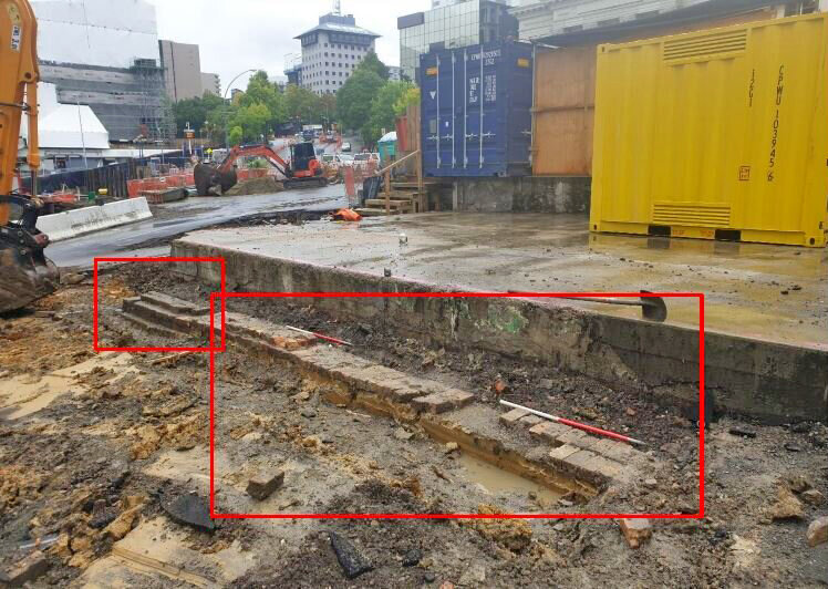   UNCOVERED: The brick wall remains abutting a clayware drain situated in concrete. The bricks were wire cut extruded and multicoloured with one glazed brick noted. The average brick measured 220mm in length x 110mm in width x  68mm in height.  