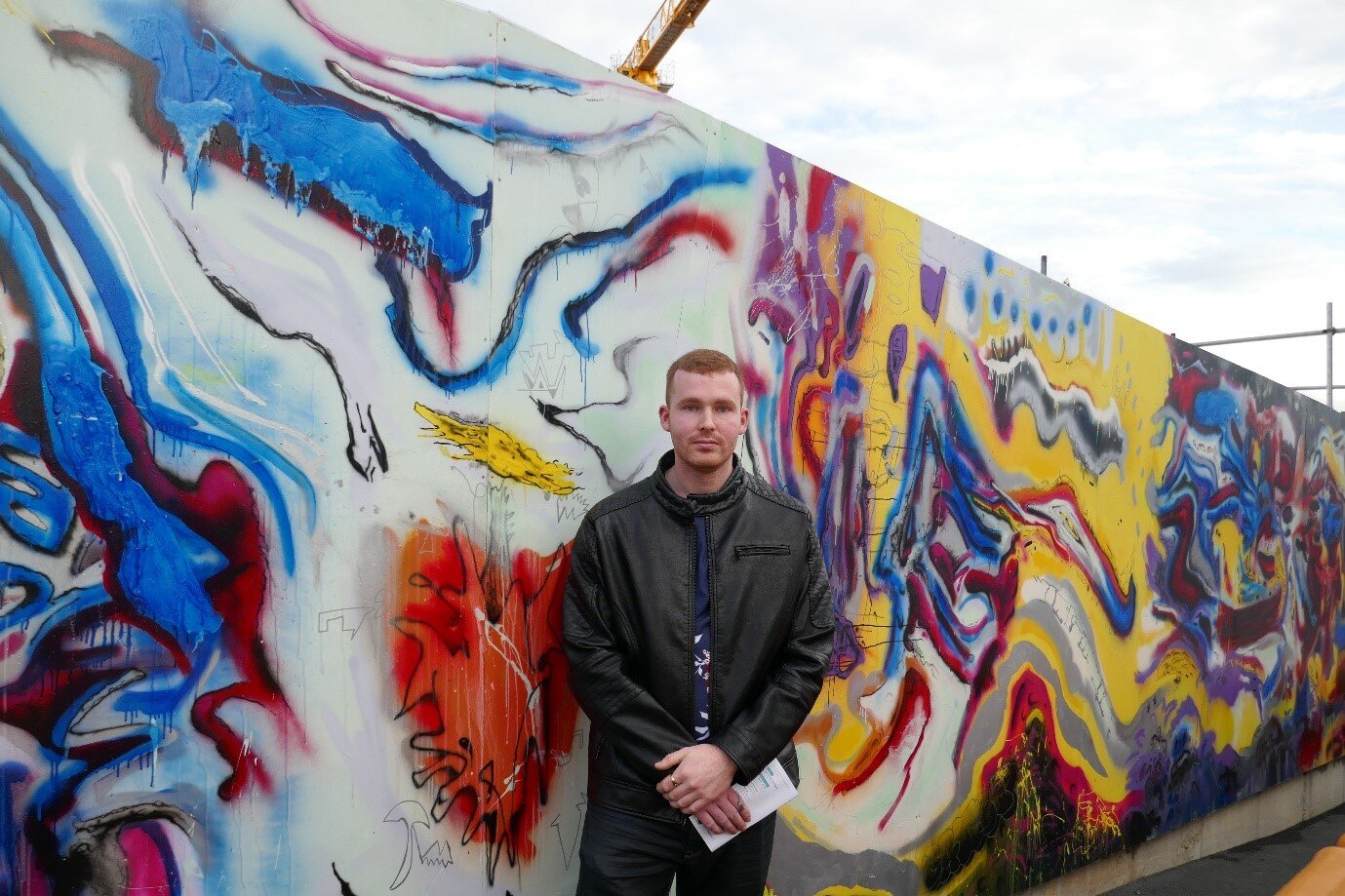  Artist Jayden Plank in front of his mural titled:  The Transcendent Flow of Maungawhau’s Energy is in All of Us.  