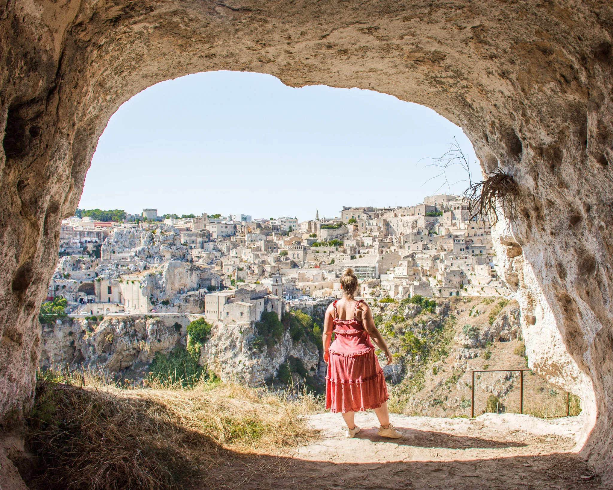 Girl in a pink dress standing in a cave looking out over Matera, Italy