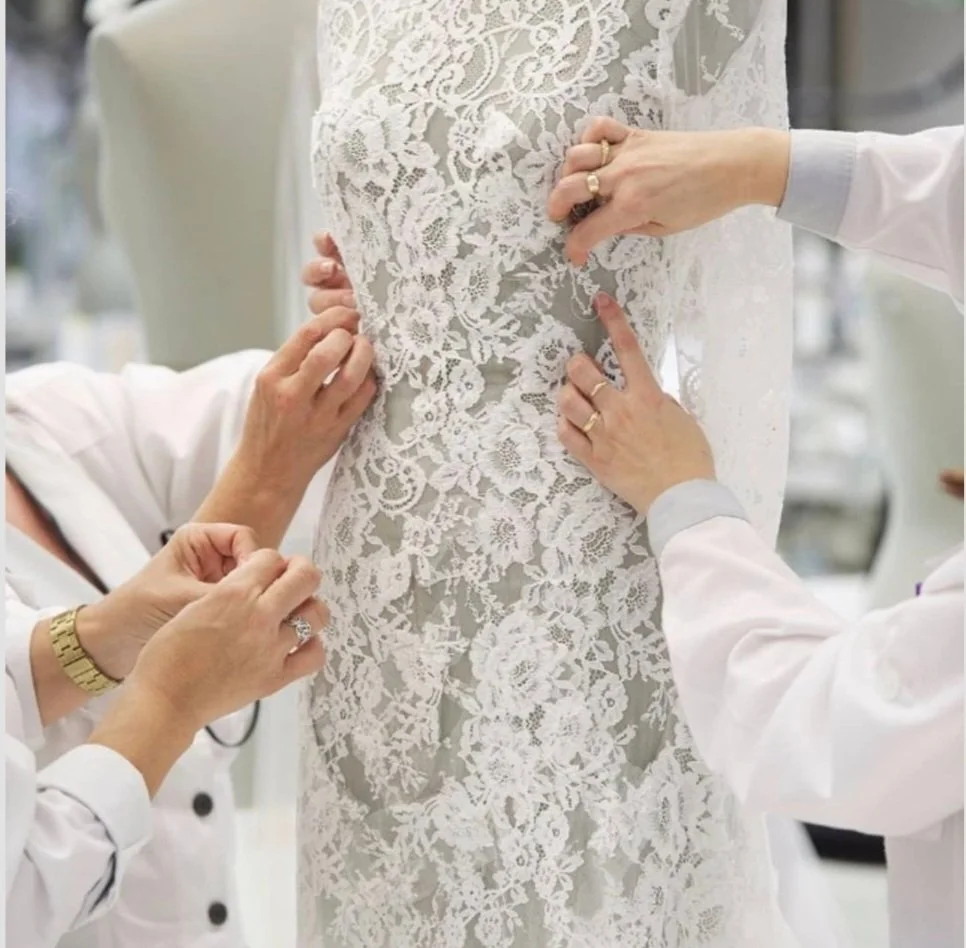 People fitting and adjusting a white lace wedding dress on a bridal mannequin.