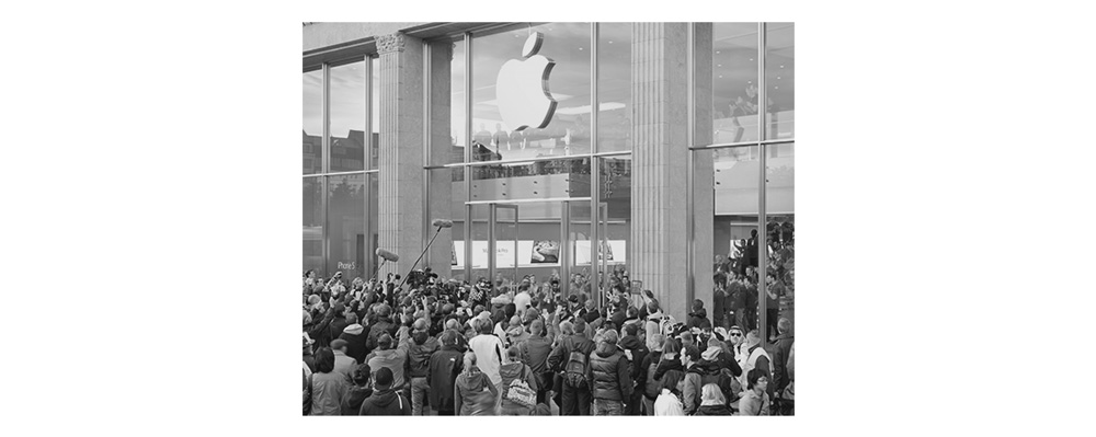 Image IV – Apple Store During the worldwide sales launch of a new smartphone, thousands of people queue up in front of the apple stores to become one of the first owners of the newest status symbol. Some camp up to two days and nights in any weather in front of the shops, just to be absolutely sure to be one of the earliest to get it. It is not uncommon to see people who get paid to be in line in order to give their place to their client moments before the doors open. When the moment arrives, the so called Apple Geniuses applaud the customers that are pouring in. The press coverage maximizes the notion of an important event. In 2012, within the first 24 hours after the launch of the 680€ priced device, more than 2 million had been sold via the internet alone.