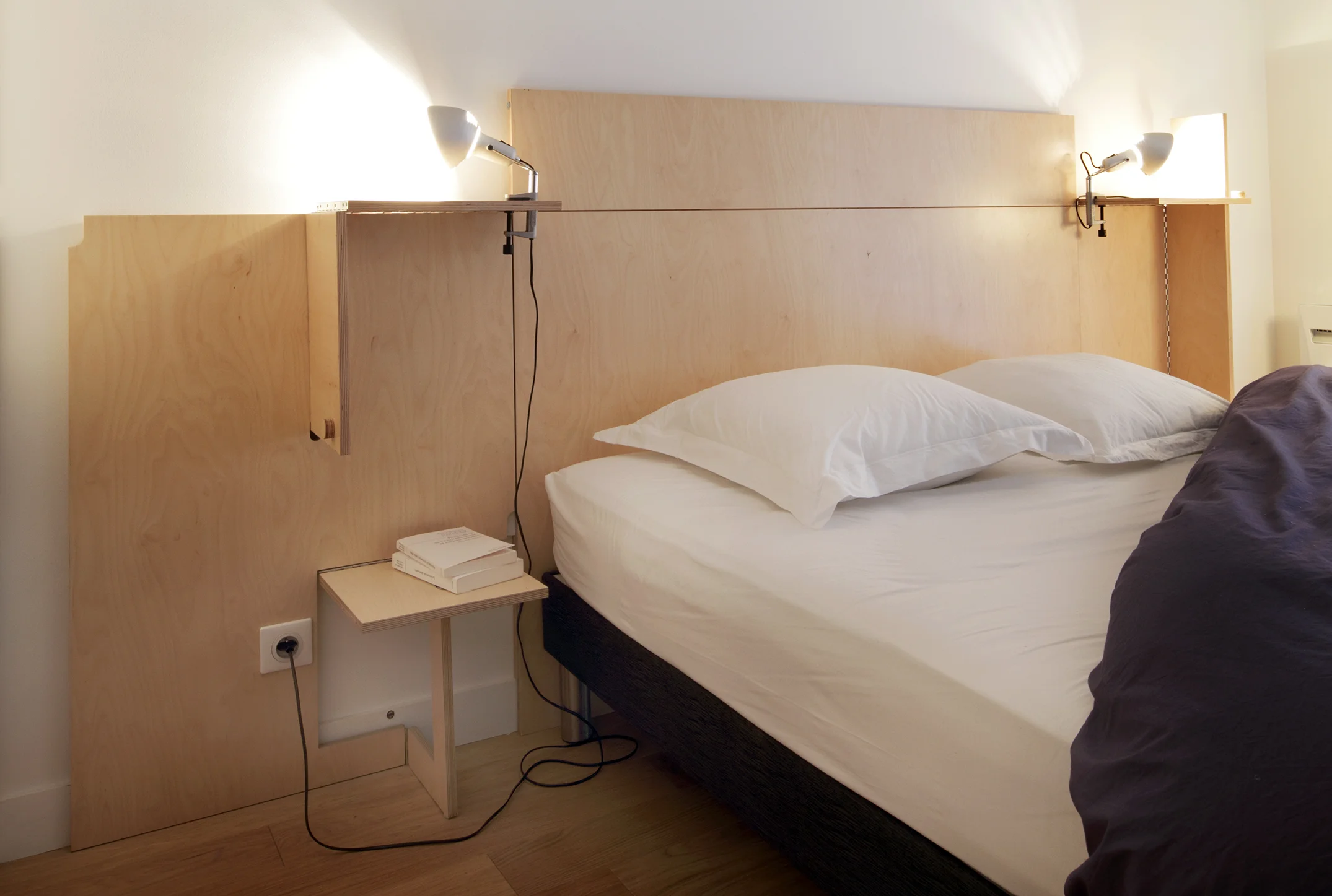 TETE DE LIT POP'UP| Création de mobilier Plus qu'une simple tête de lit ayant pour objectif de protéger le mur, la «TL Pop-up» sert à la fois de tête de lit mais se transforme aussi en chevets et en étagères au gré des envies. L'idée étant d'utiliser un panneau de bois dans sa totalité, en supprimant les chutes. Conçue à la manière d'un pop'up, avec des éléments qui se déploient, cette tête de lit est découpée au jet d'eau pour ne pas perdre de matière. Des charnières à piano permettent de faire pivoter les différents éléments. Des trous et des fentes, ménagés dans les panneaux, suffisent à les liaisonner entre-eux.