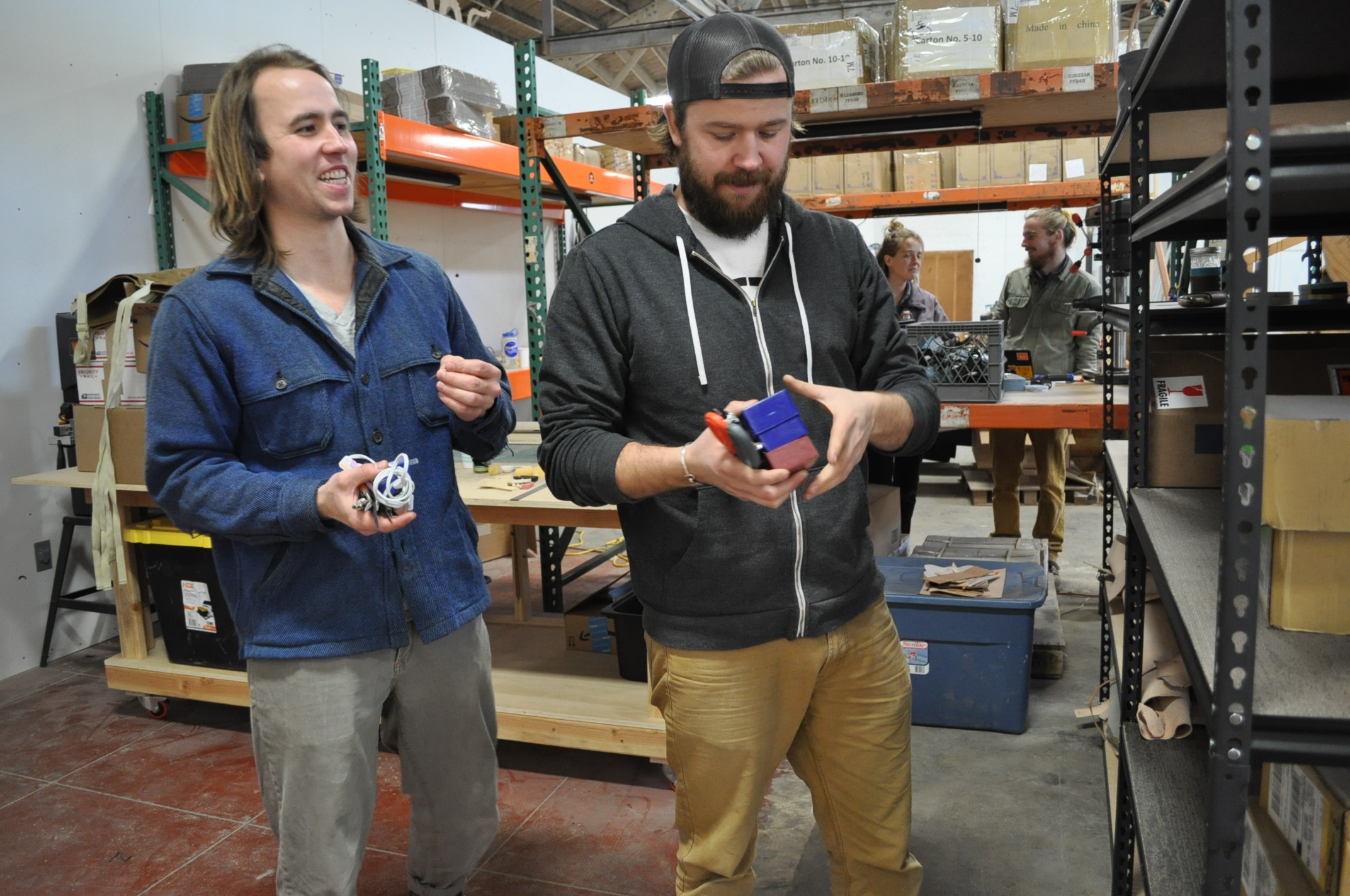 Adam (left) and Jason Gorske of DIY Bar organize storage shelves in their Annex workstation, while Hannah Teagle and Bar Smith of Maslow CNC chat in theirs.