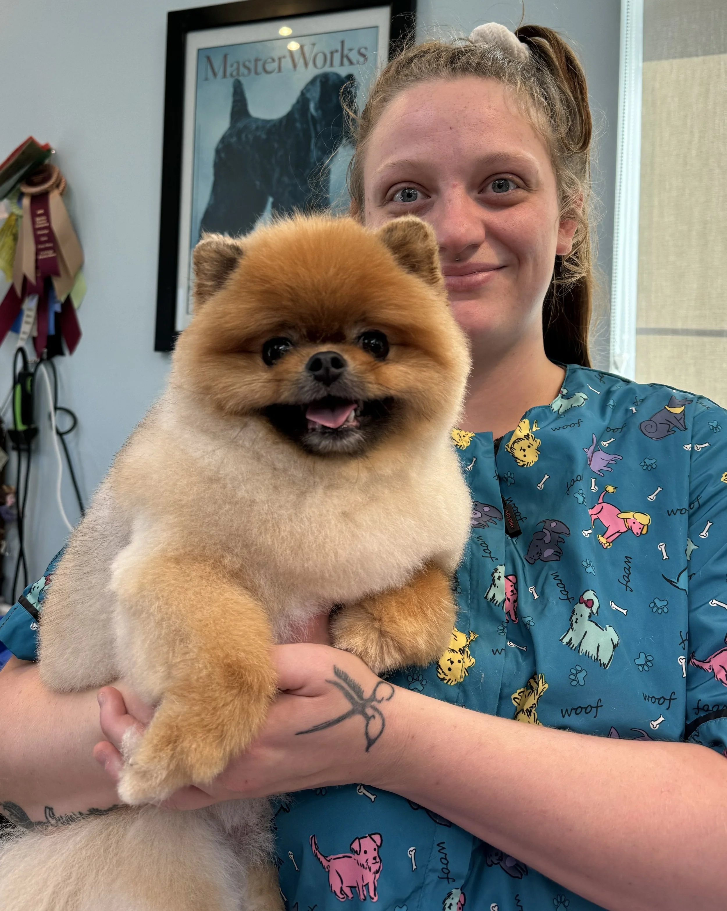A woman in a blue Vet staff uniform holding a smiling Pomeranian dog inside a veterinary clinic.