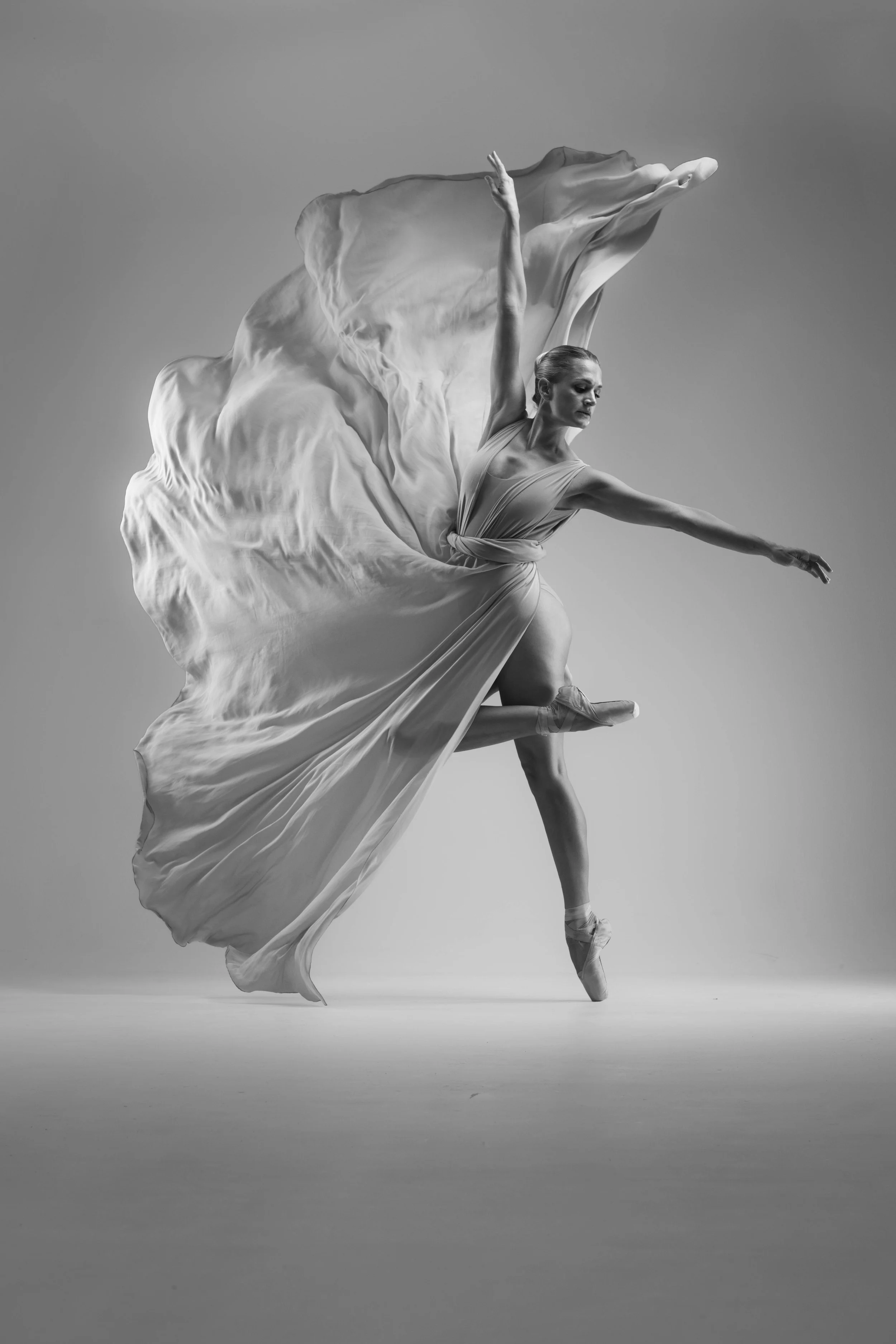 A ballerina in a flowing dress performing on pointe, captured in black and white with dramatic movement.