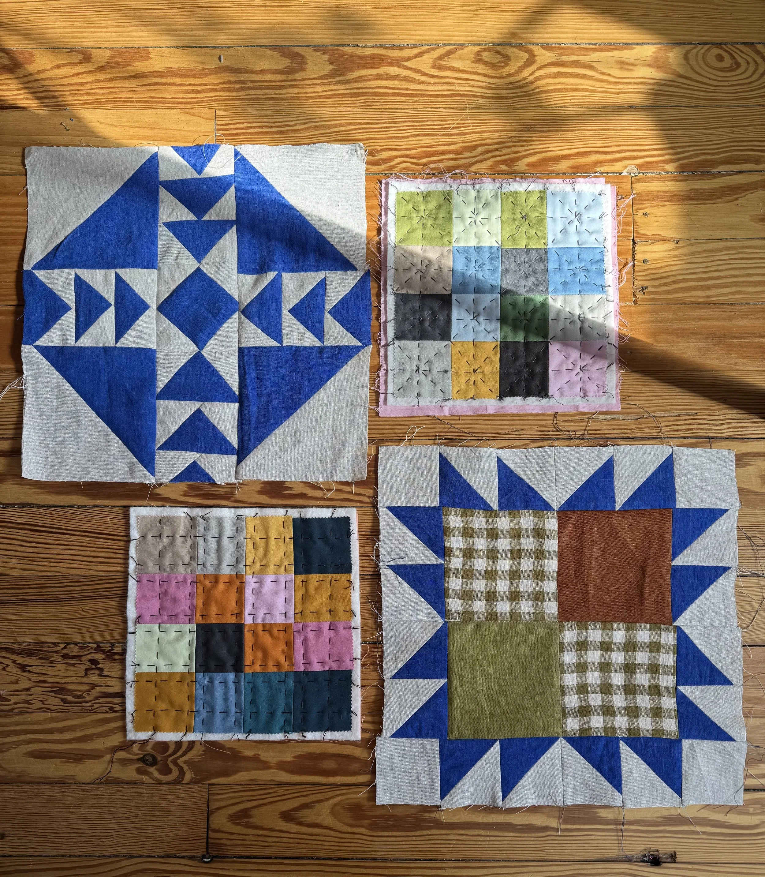 Two traditional quilt blocks and two mini quilts  by textile artist Rachel Connor lay on a wood floor in the sunlight