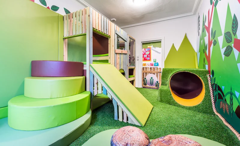 The timber play structure is surrounded by artificial lawn turf, offering a contemporary aesthetic.
