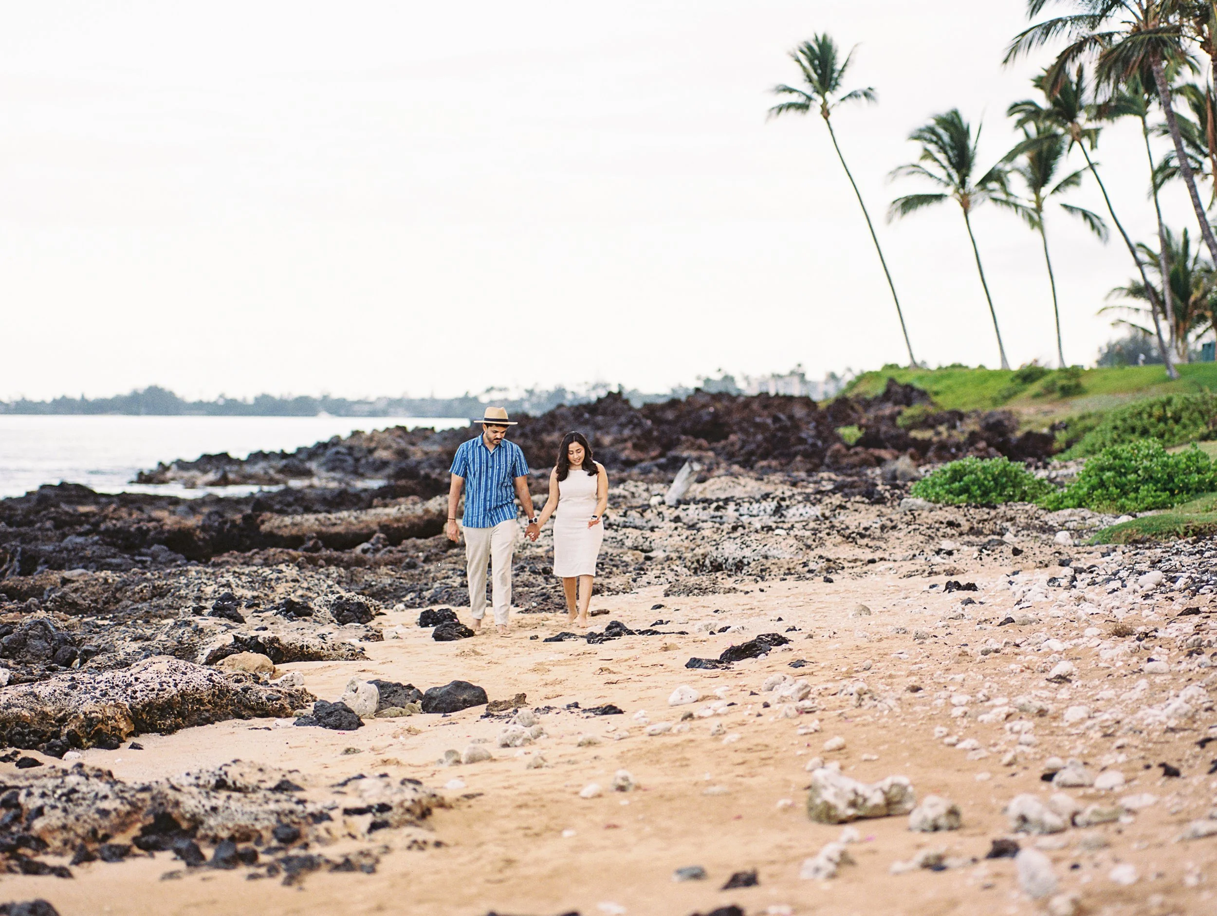 A couple newly engaged holding hands walking Keawakapu Beach in the early morning on Maui.
