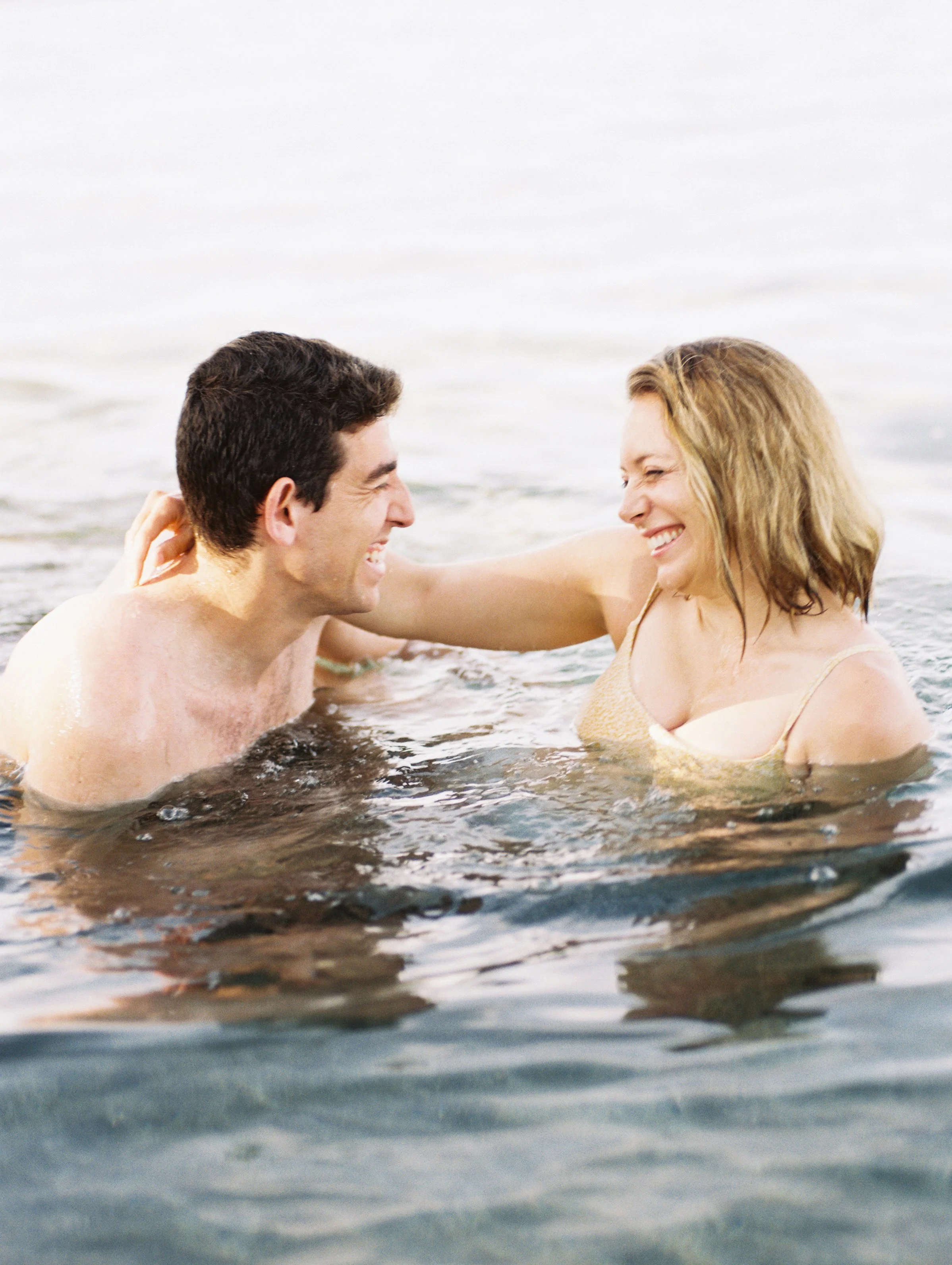 A couple photographed in the ocean in Lahaina Maui laughing captured using film photography.