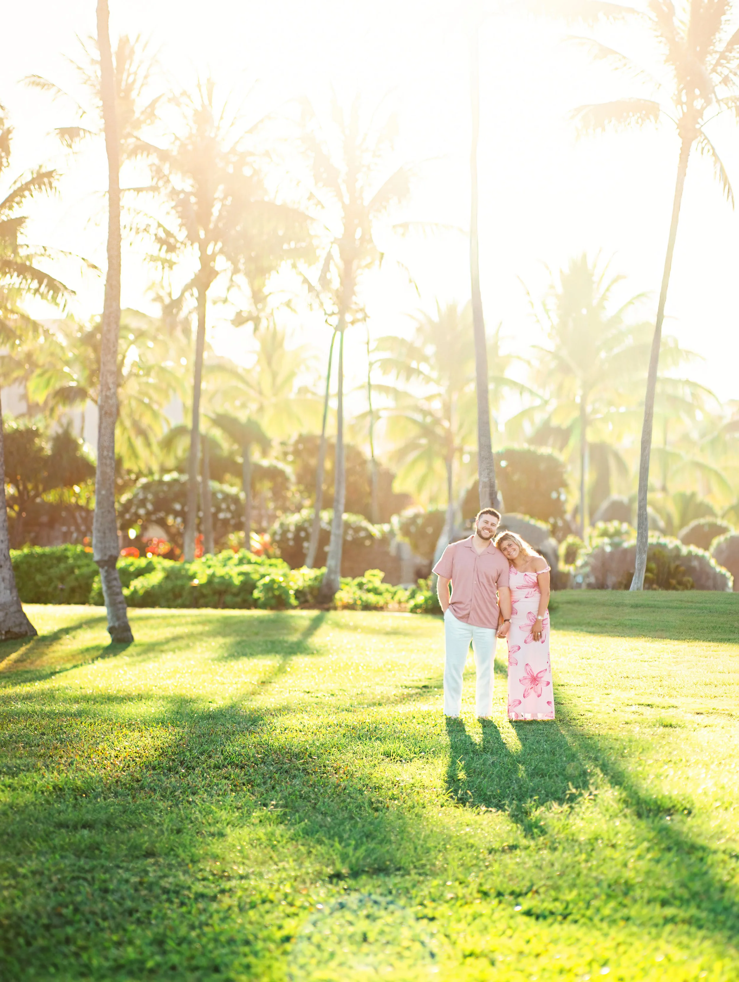 A couple standing together underneath palm trees at The Montage above Kapalua Bay in Maui.