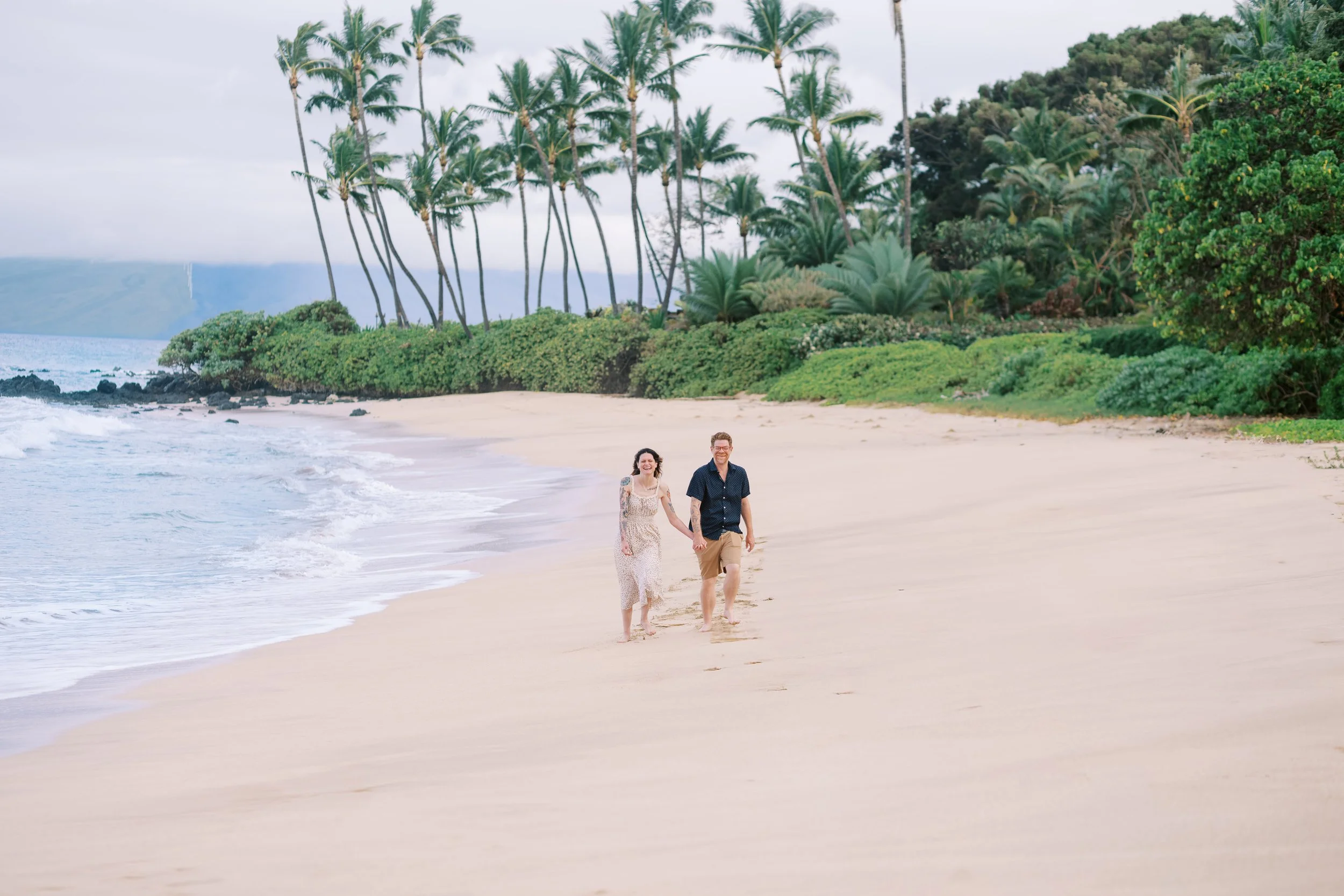 A couple walking on the sandy shoreline in Wailea for a photoshoot in Maui at sunrise.