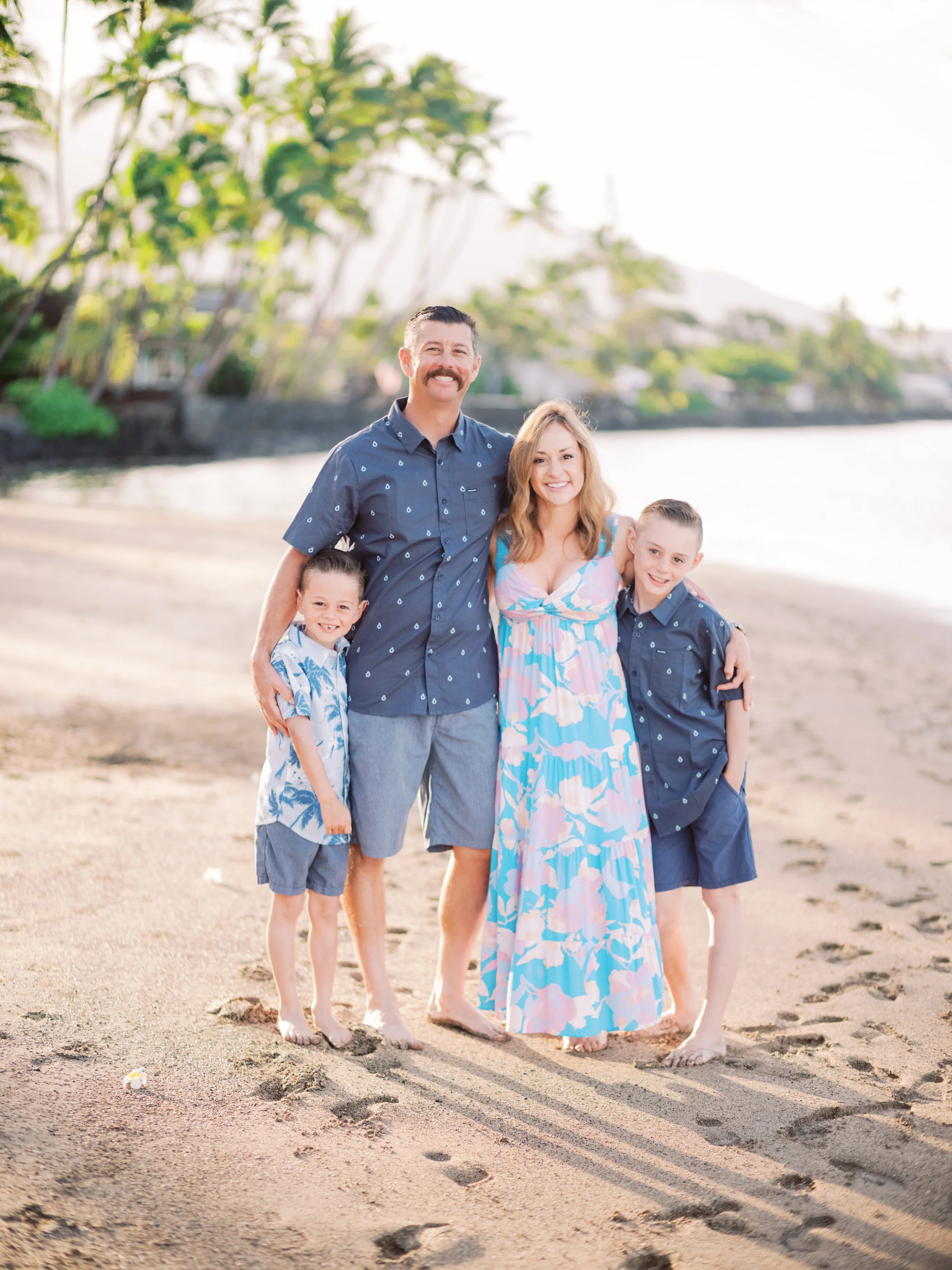 A family smiling on a tropical beach in Maui during the early morning with palm trees in the background