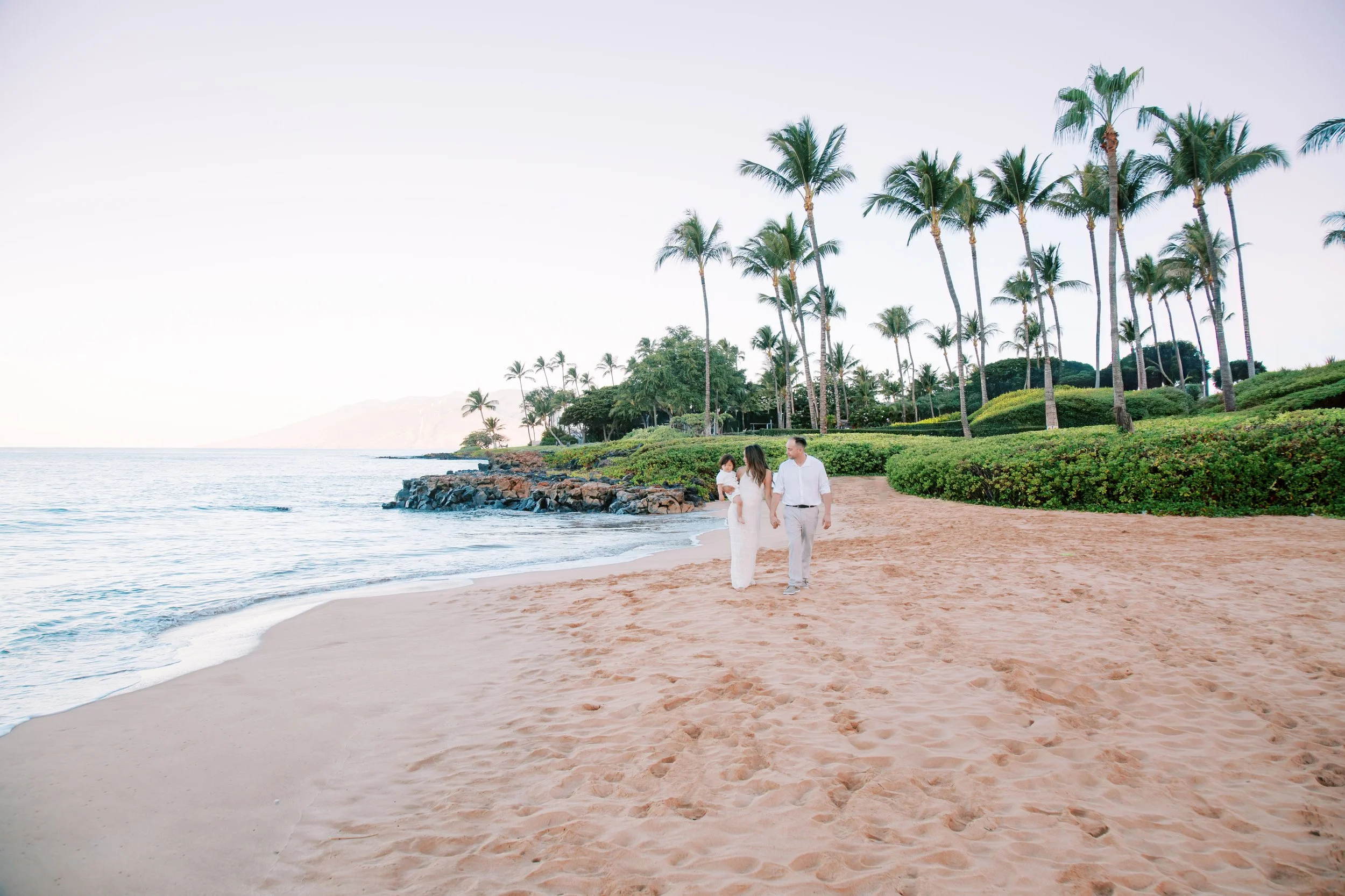 A family with a young toddler holding hands walking Wailea Beach in the early morning during a family photoshoot on Maui.