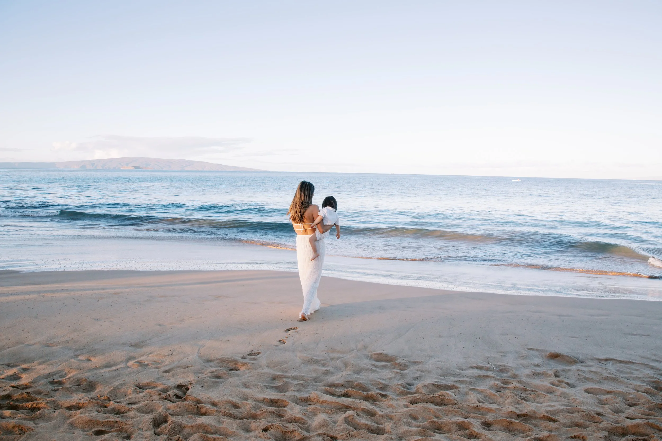 A mother holding her young toddler while at the ocean's edge on Wailea Beach in Maui.