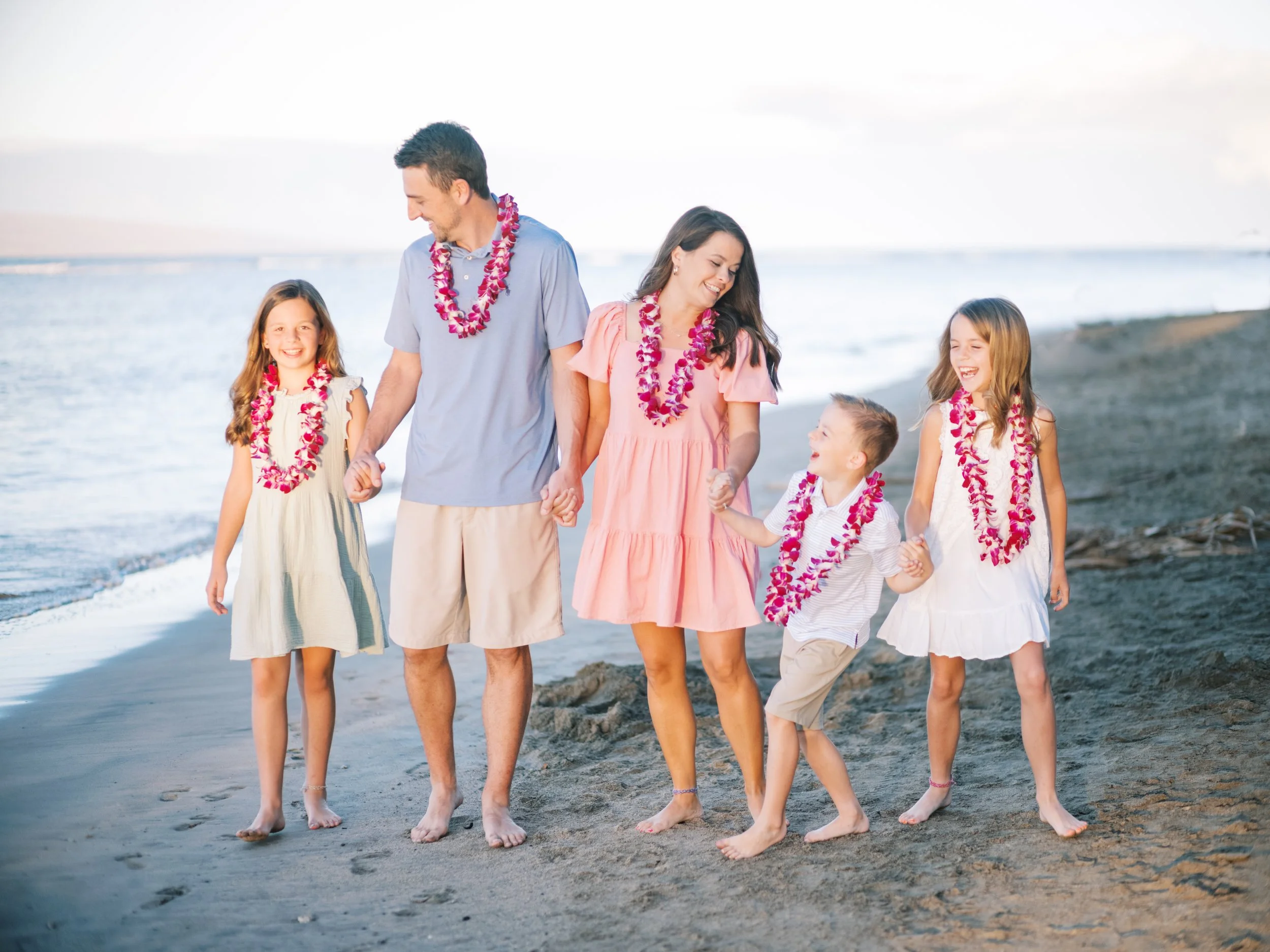 A family barefoot laughing on the beach in the early morning during a Maui family photoshoot in Lahaina.