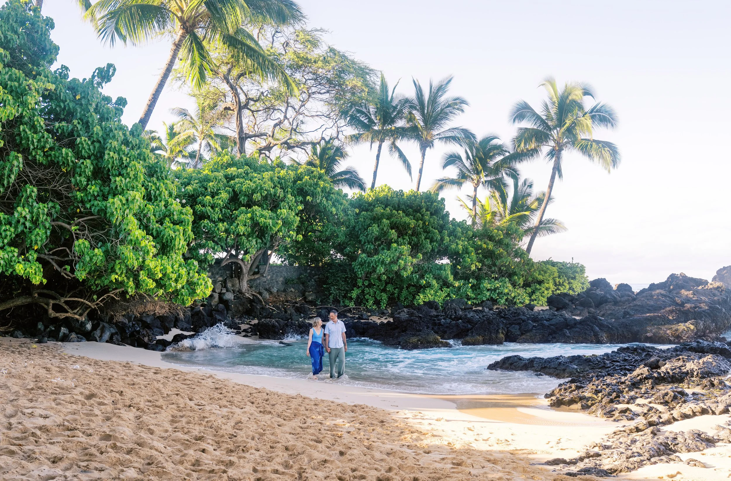 A couple walking on the shoreline at sunrise at Makena Cove on Maui.