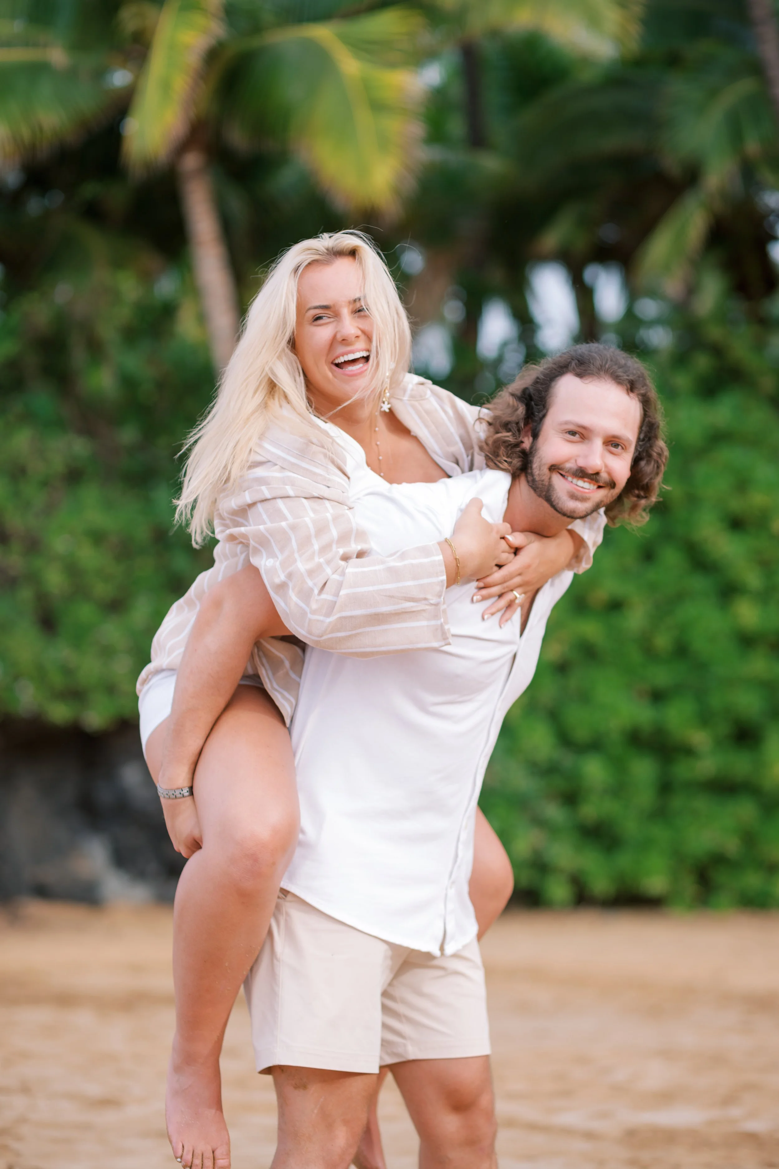 A couple laughing during an engagement photoshoot with tropical palm trees behind them in Wailea Maui.