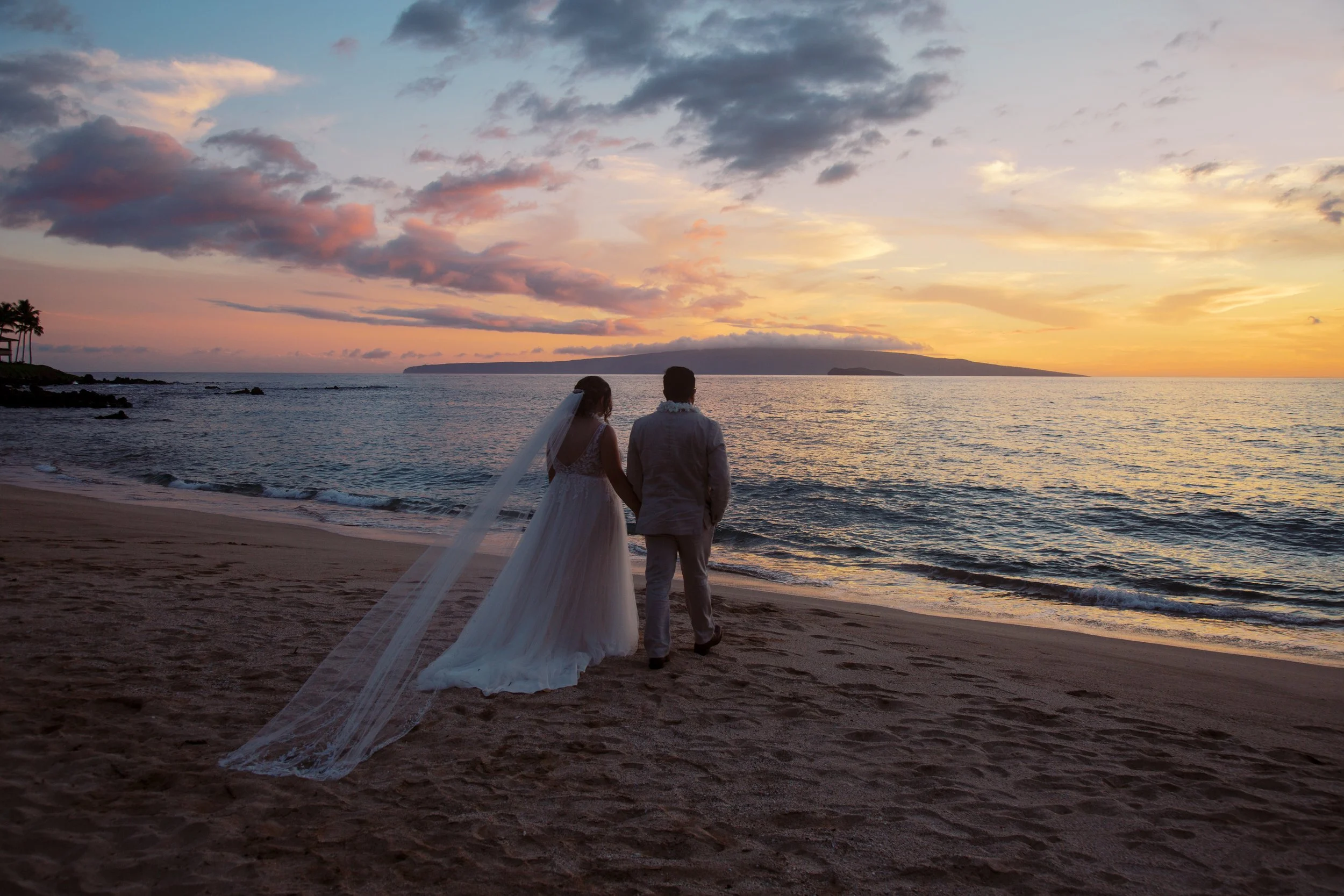 A vibrant sunset elopement of a couple standing on Palauea Beach ( White Rock ) in Maui Hawaii.