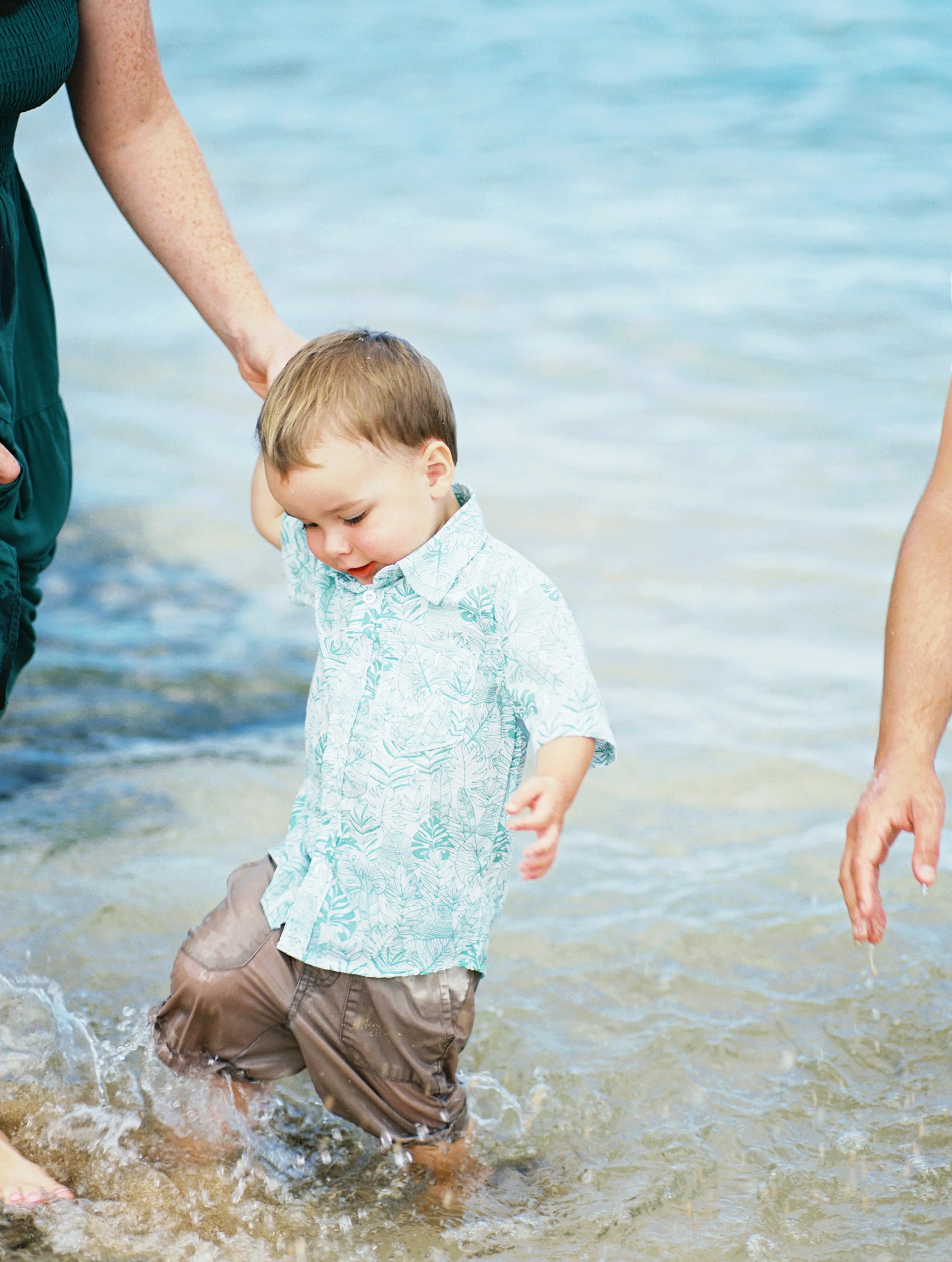A toddler playing in the bright blue ocean water in Kapalua Maui during a morning photoshoot