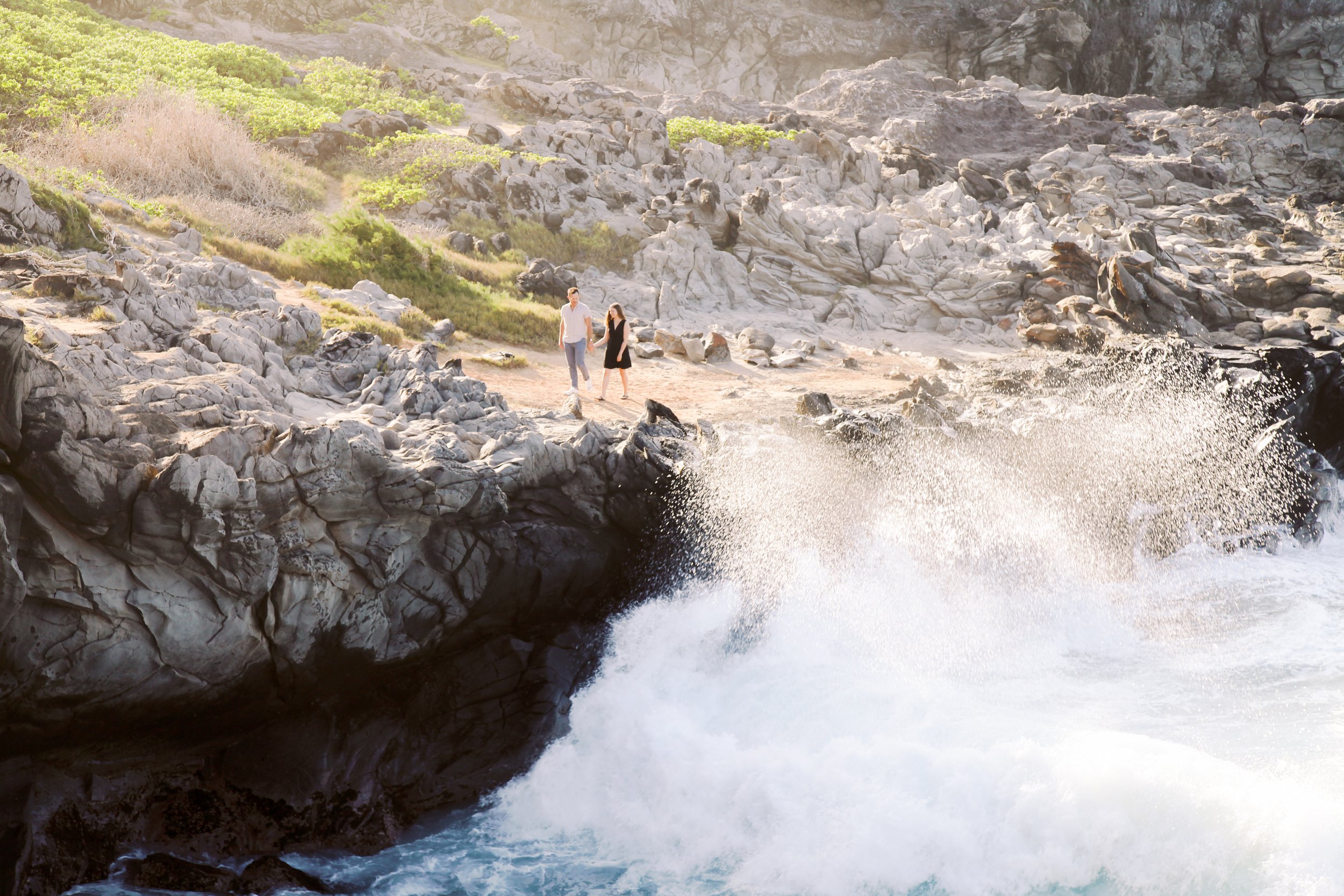A couple walking above the sea cliffs in Ironwoods Kapalua with waves dramatically crashing below them.