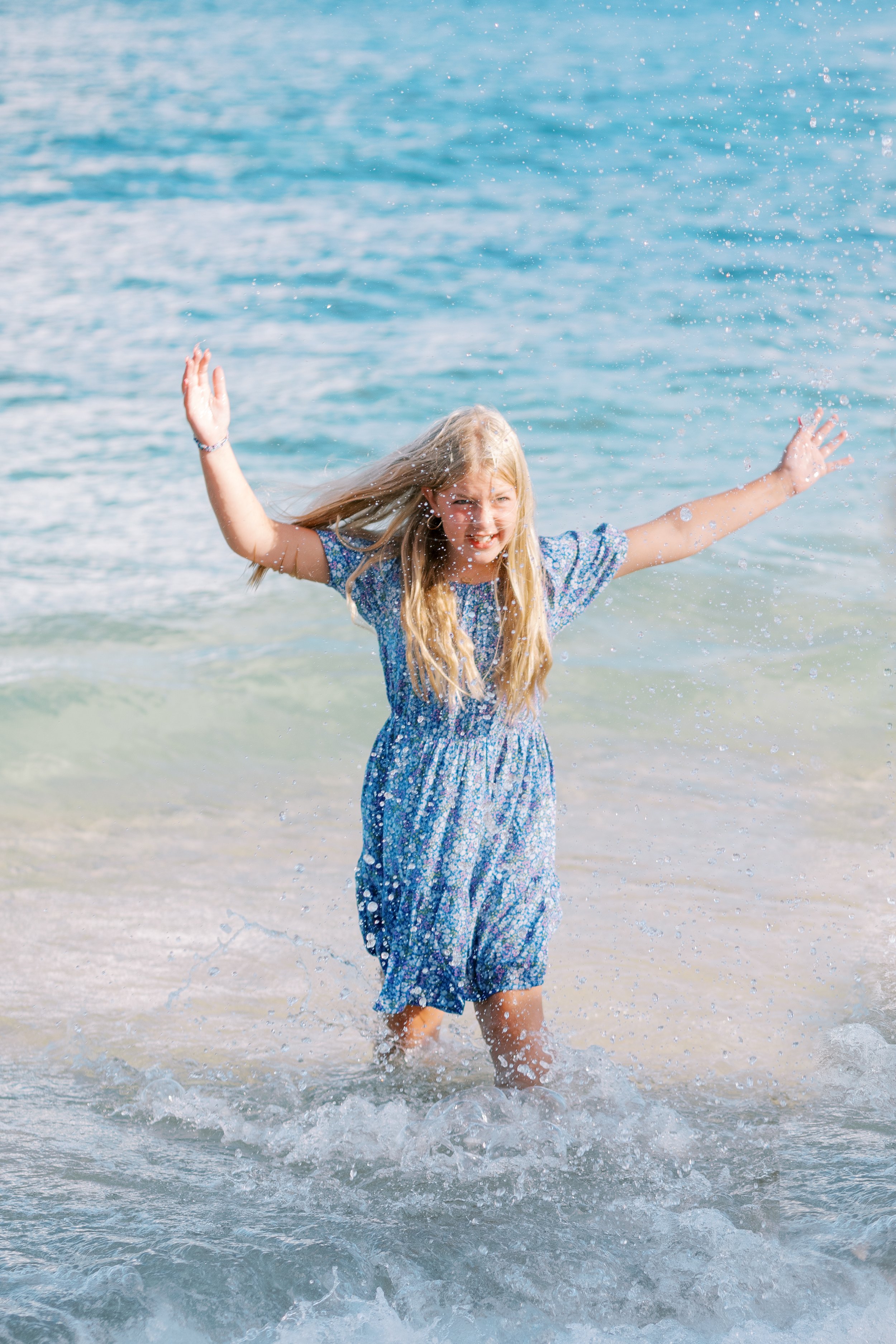 A young girl splashing in the ocean at Kapalua Bay during a family photoshoot.