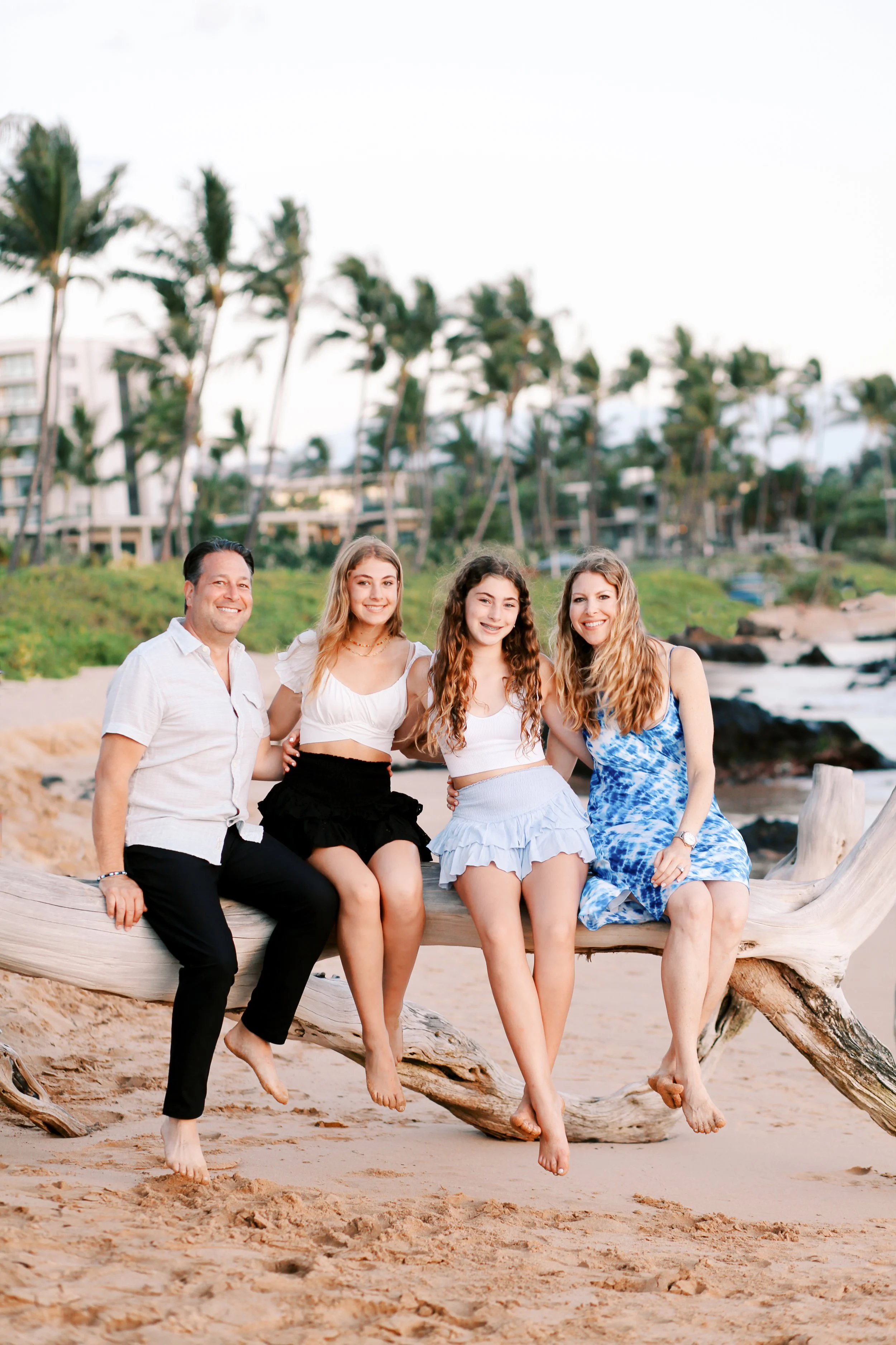 A family sitting on a log in front of The Andaz on Maui in Wailea during a sunset family photoshoot.